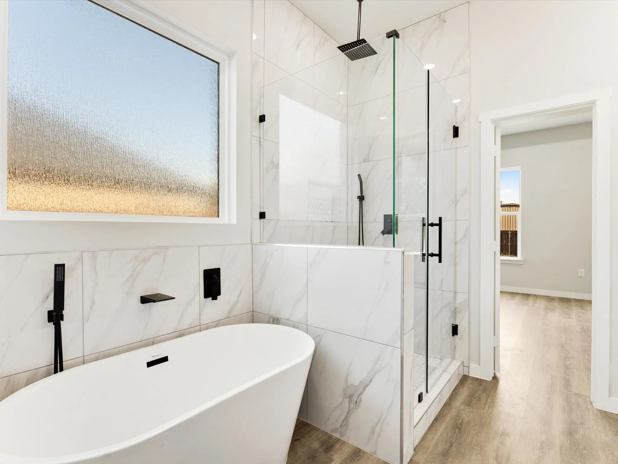 Spa-inspired primary bathroom featuring a freestanding soaking tub, walk-in shower with frameless glass enclosure and rainfall showerhead, marble subway tile surround, matte black hardware fixtures, and polished concrete flooring