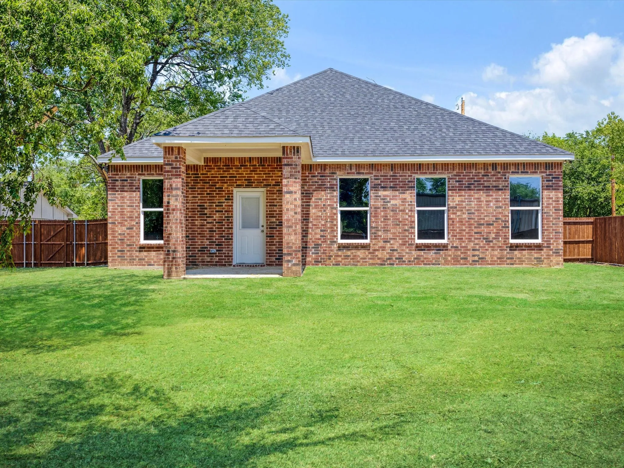 Brick exterior with a dark shingle roof, complemented by white window frames, a rear entry door, and a private wooden fence