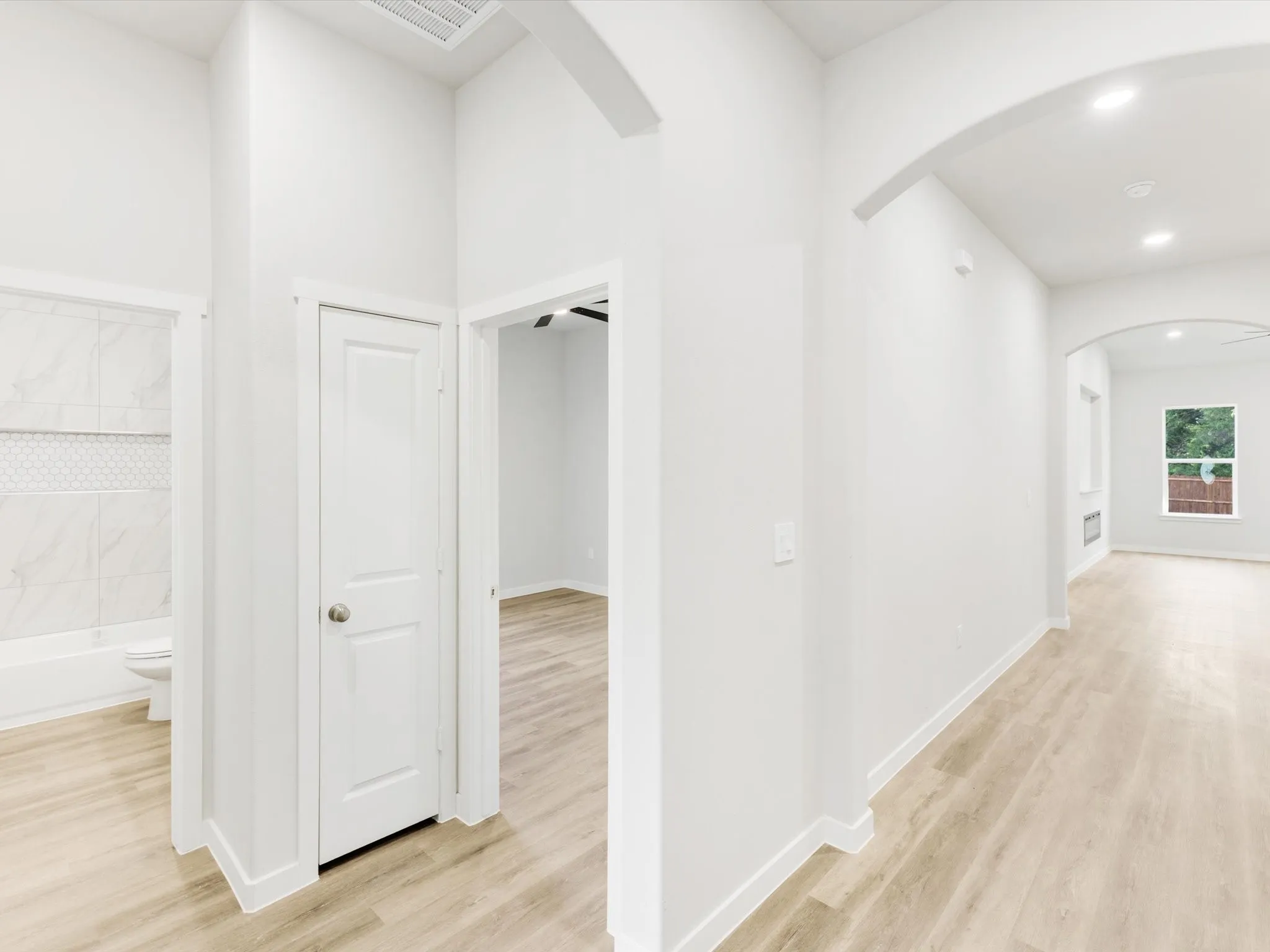 Wood-finish flooring throughout, bright white walls, recessed lighting, arched doorways, and a bathroom featuring a tiled shower and tub