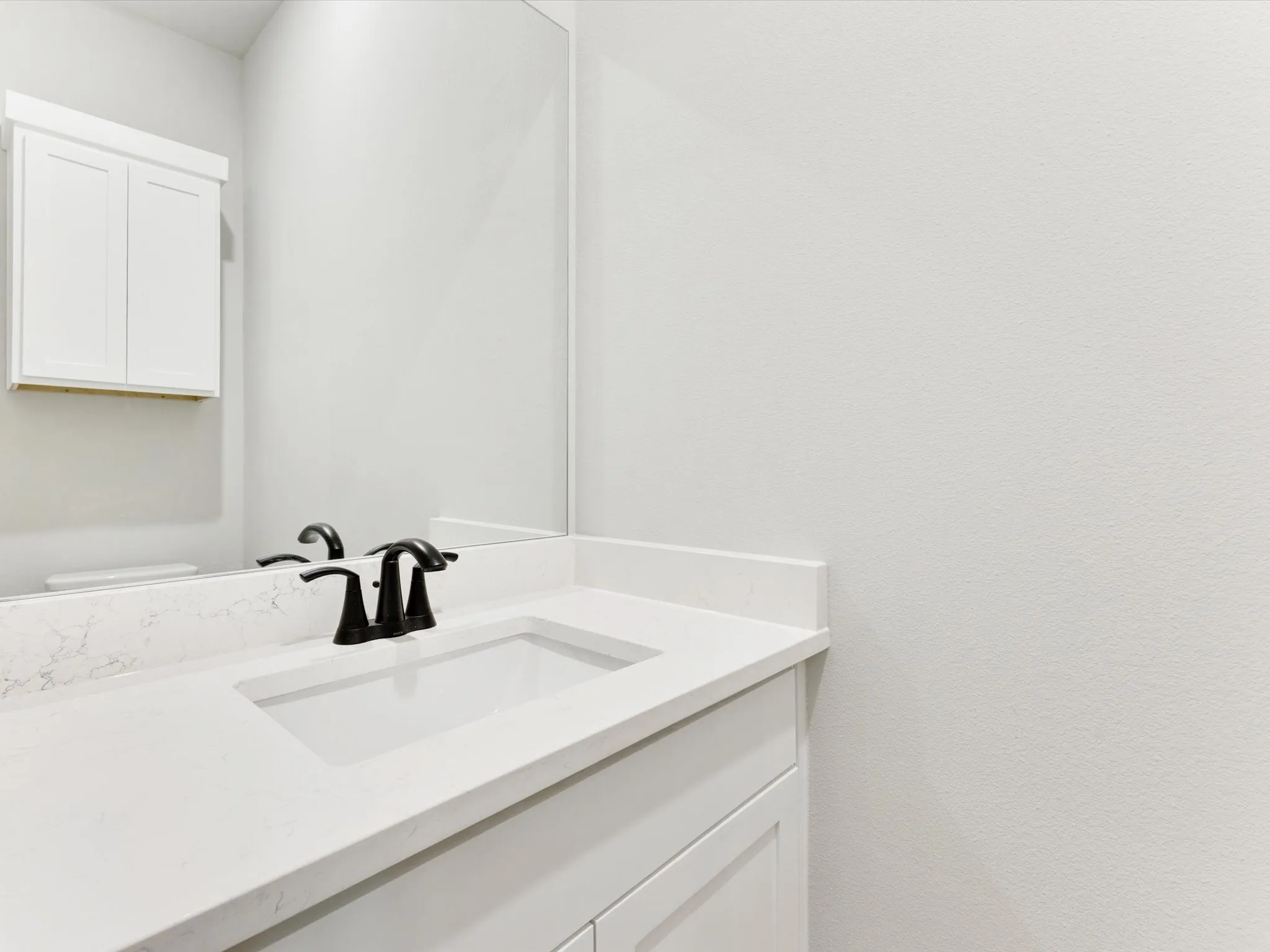 White vanity with integrated sink, sleek black faucet, and a wall-mounted medicine cabinet