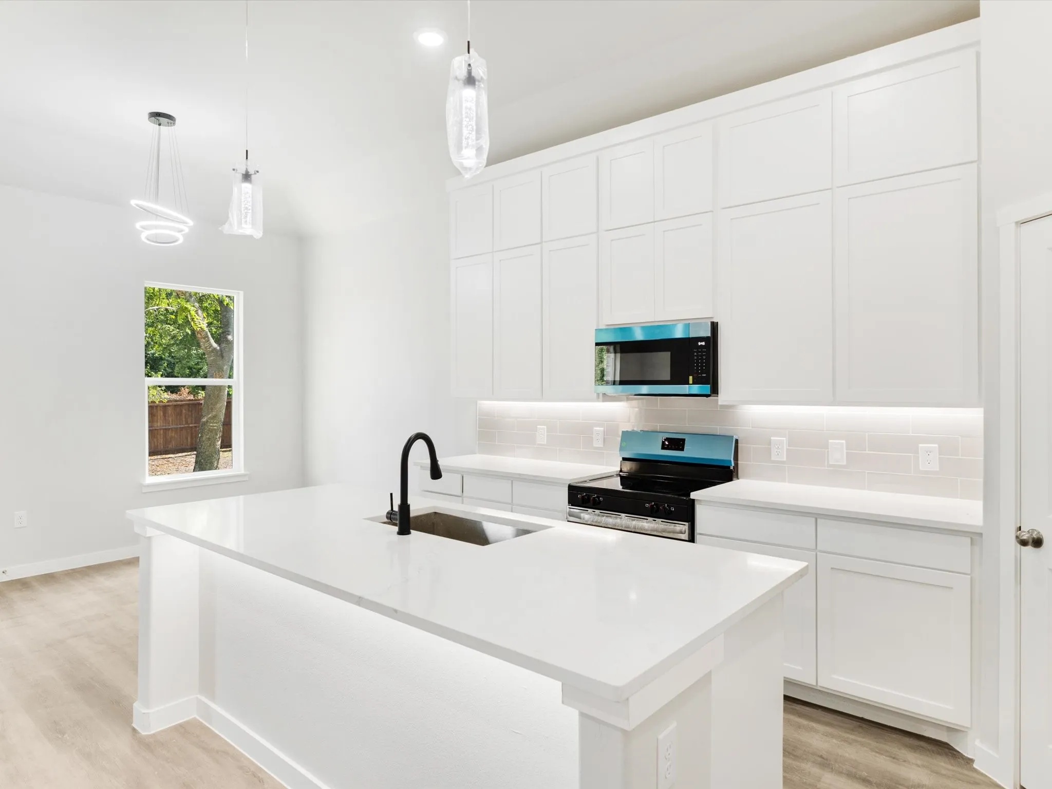 Kitchen featuring white shaker cabinetry, an island with an integrated sink, quartz countertops, and pendant lighting
