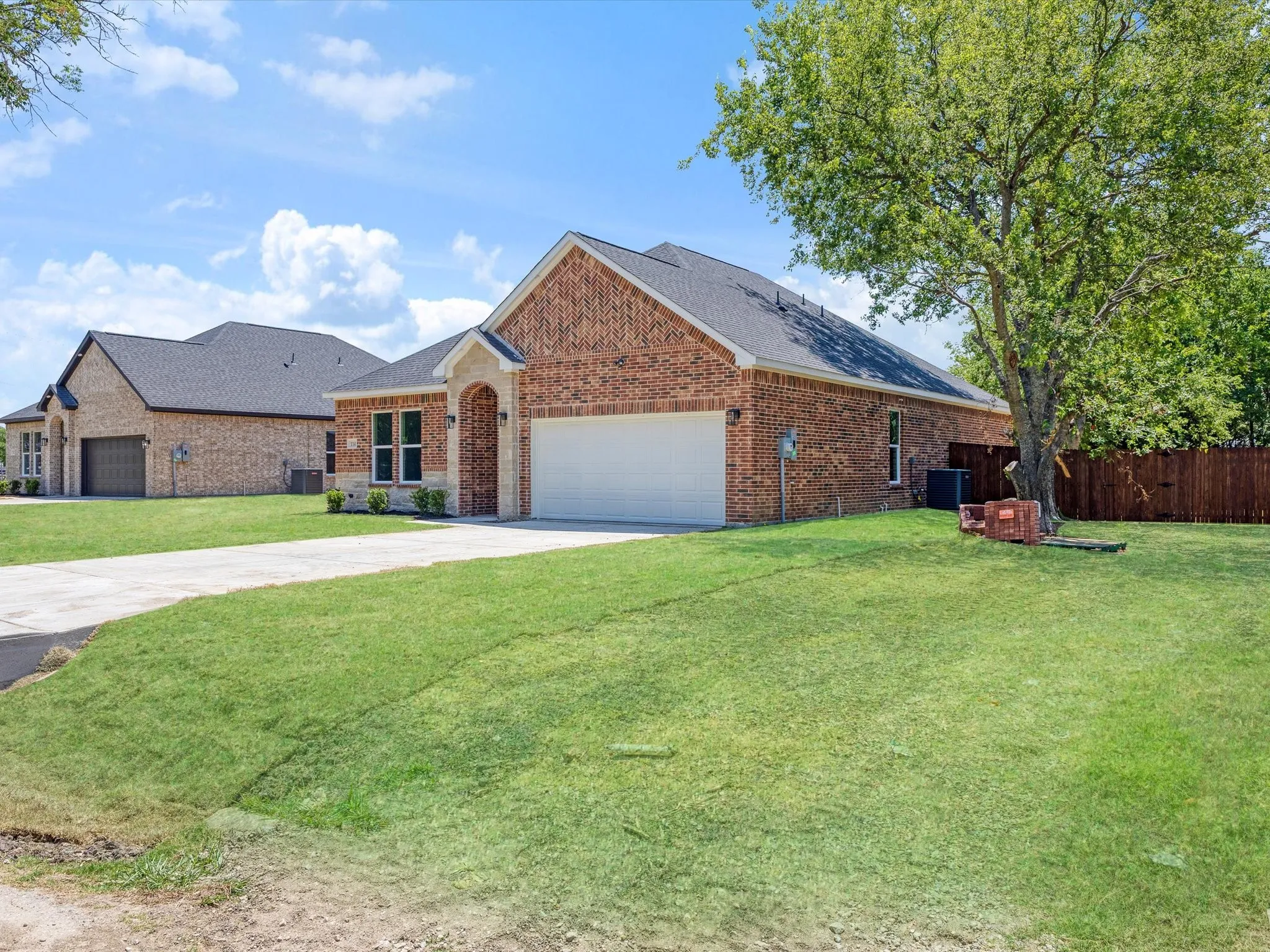 Brick exterior with stone accents, attached two-car garage, concrete driveway, and a mature tree