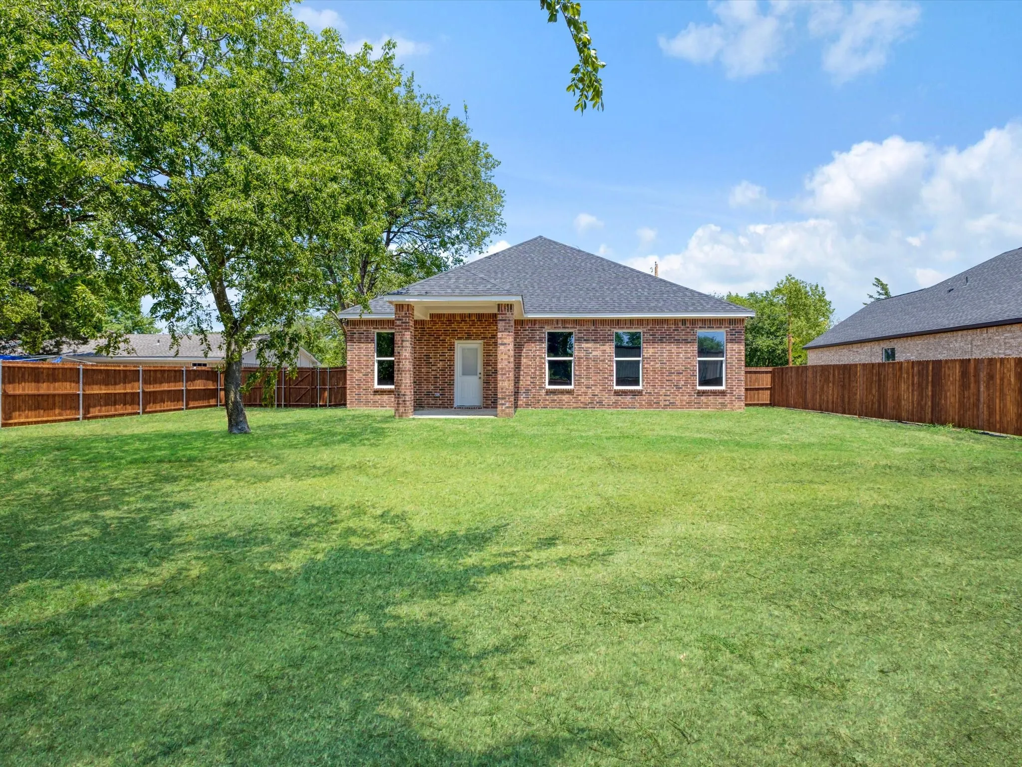 Expansive backyard with a manicured lawn, full privacy fencing, and mature trees