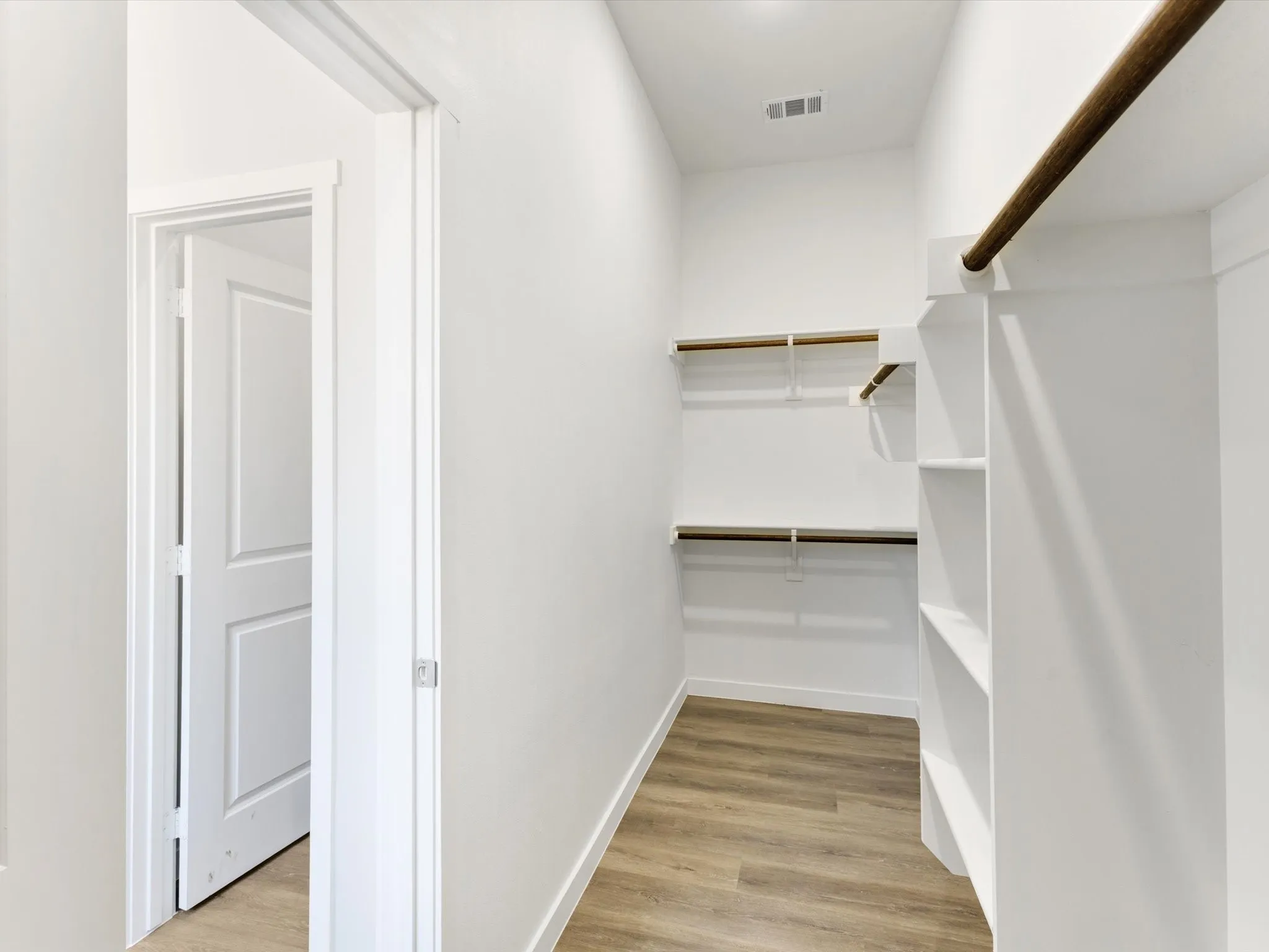 Walk-in closet featuring wood-finish flooring, built-in shelving, and multiple hanging rods
