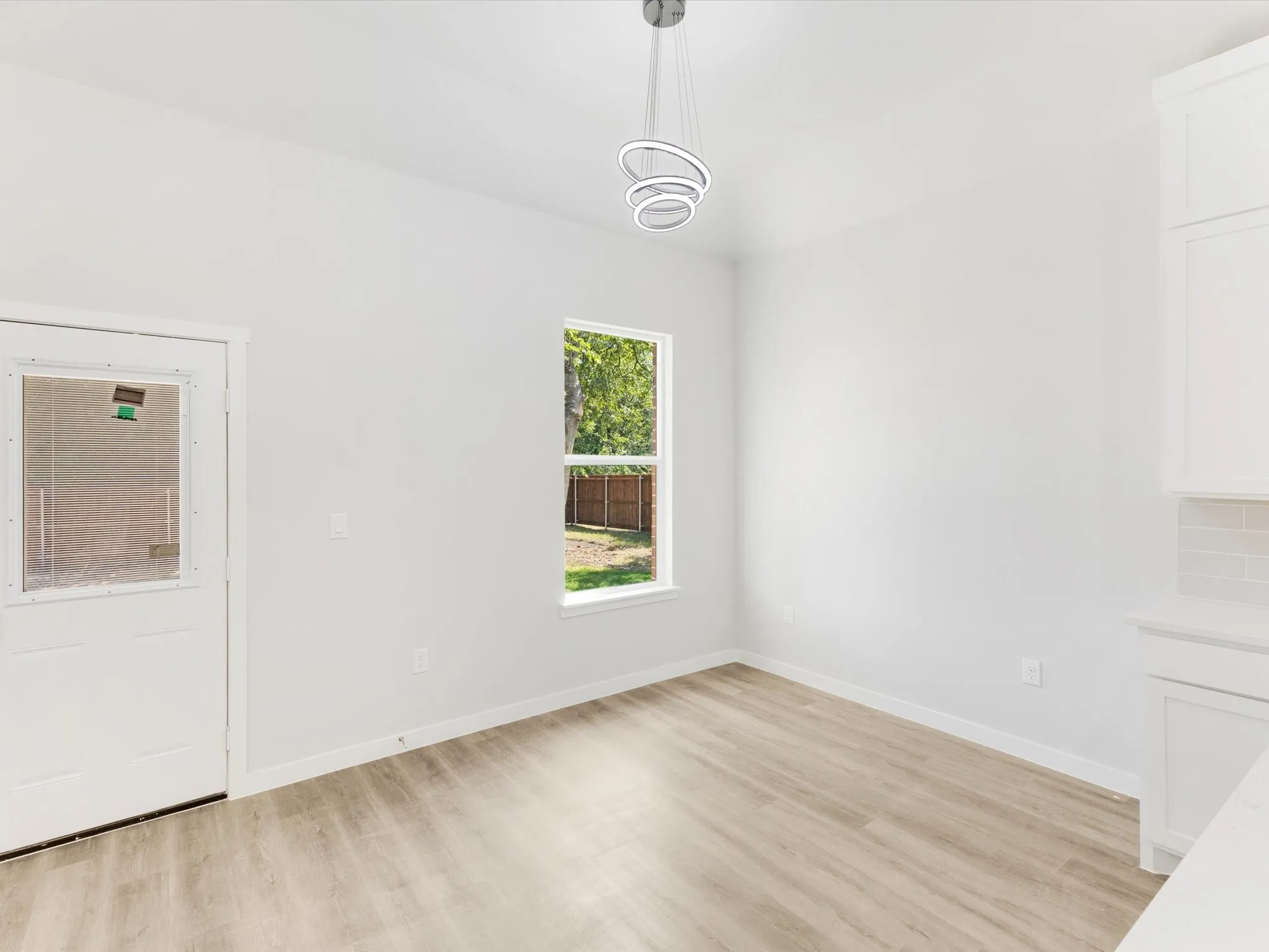 Recessed window with exterior views, wood-finish flooring, contemporary ceiling light fixture, white cabinetry, and subway tile backsplash