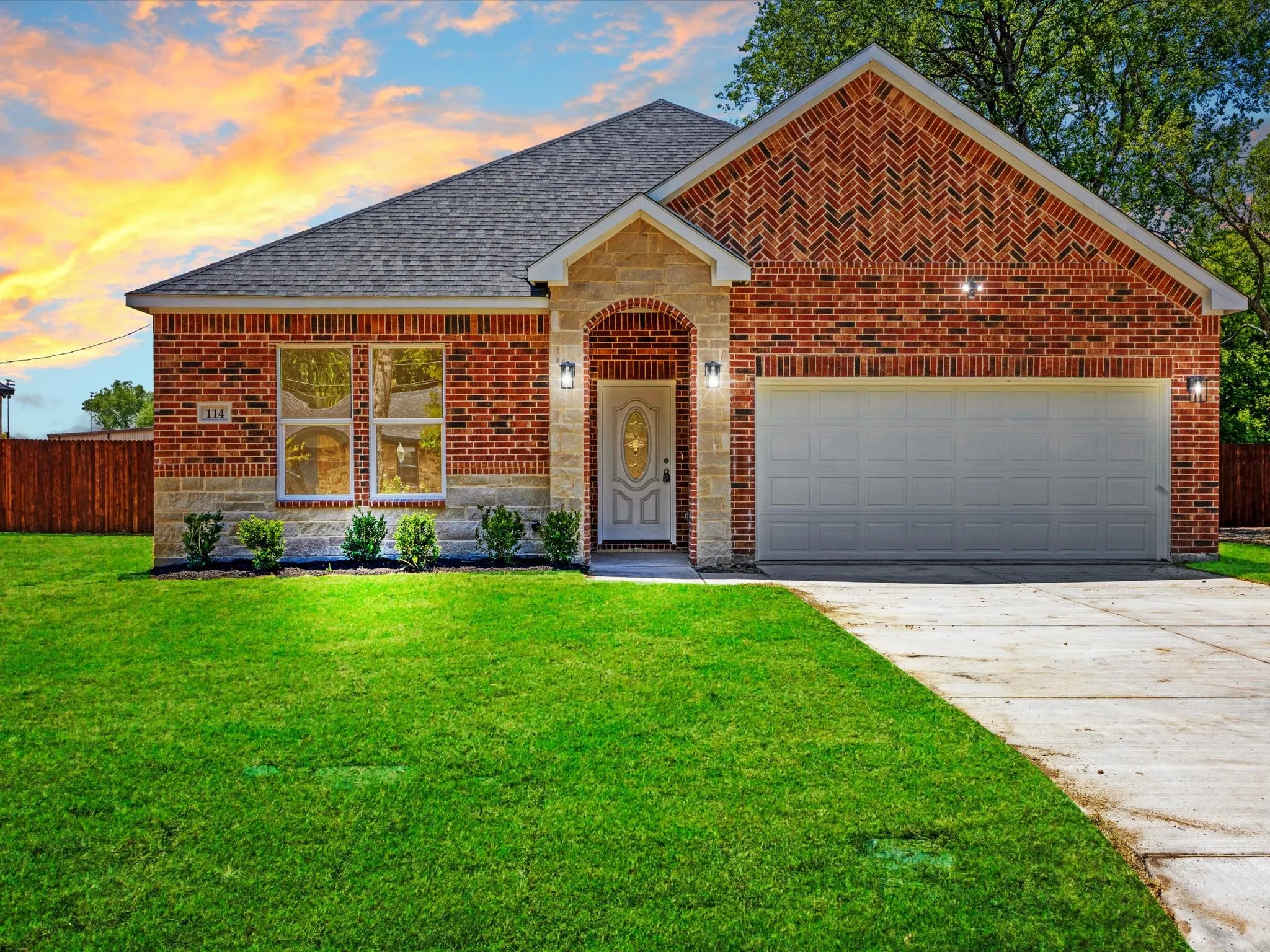 Brick exterior with stone accents, arched entry, attached two-car garage, concrete driveway, and a front yard with manicured landscaping