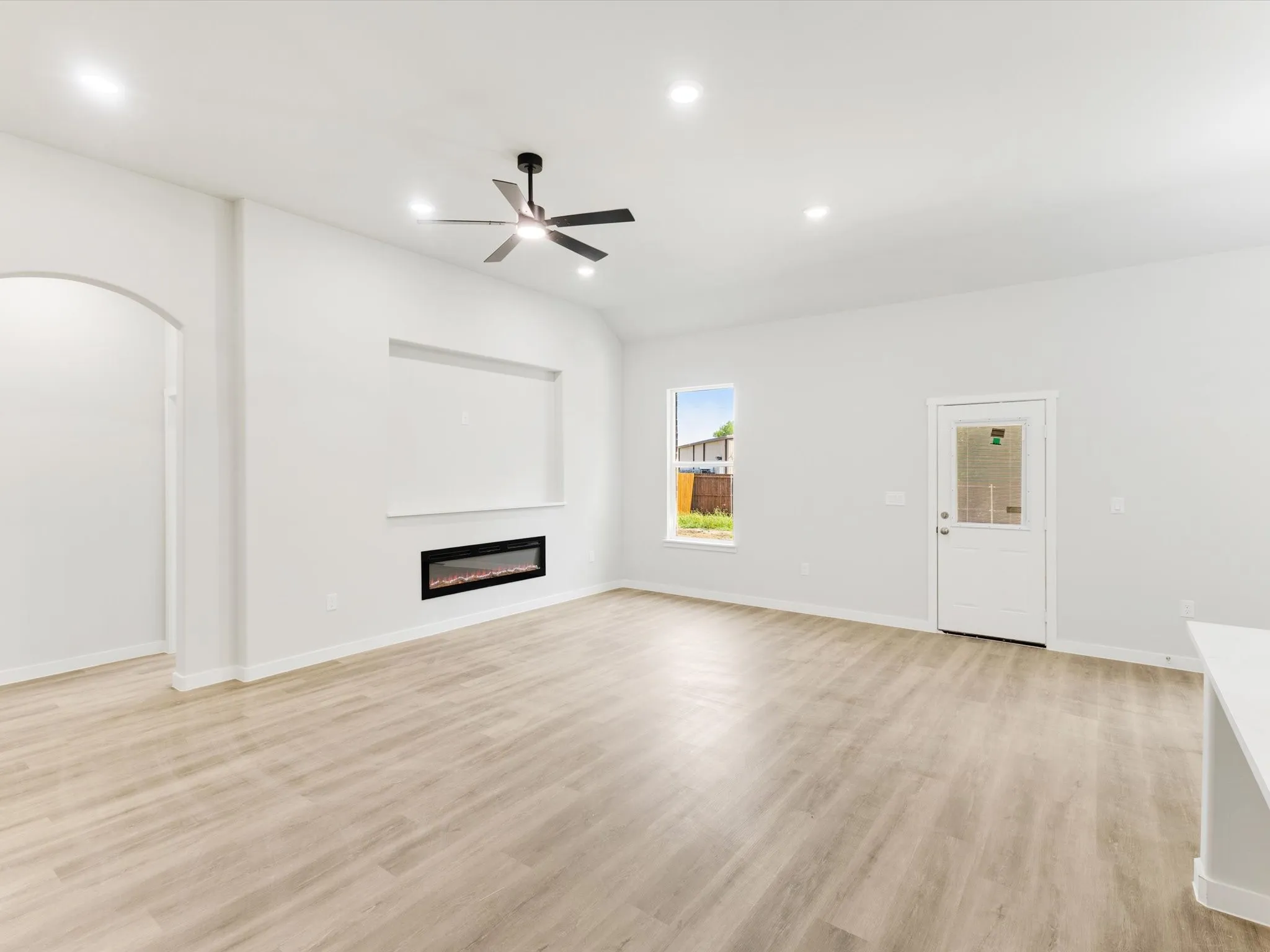 Spacious living area featuring wood-finish flooring, an electric fireplace with an integrated media niche, an arched entryway, recessed ceiling lighting, and a ceiling fan