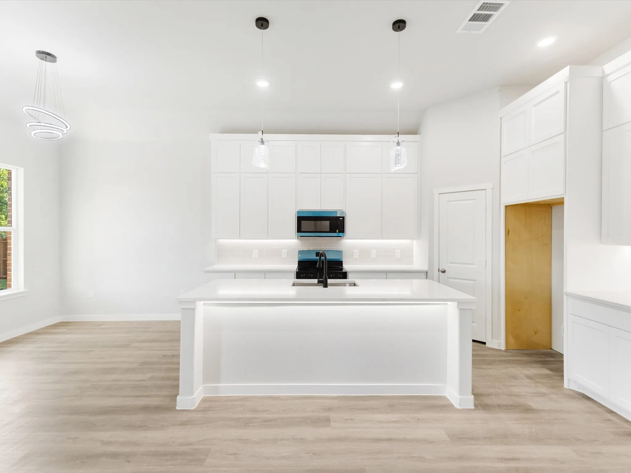Open-concept kitchen featuring an island with integrated lighting, white cabinetry, integrated microwave, and wood-finish flooring