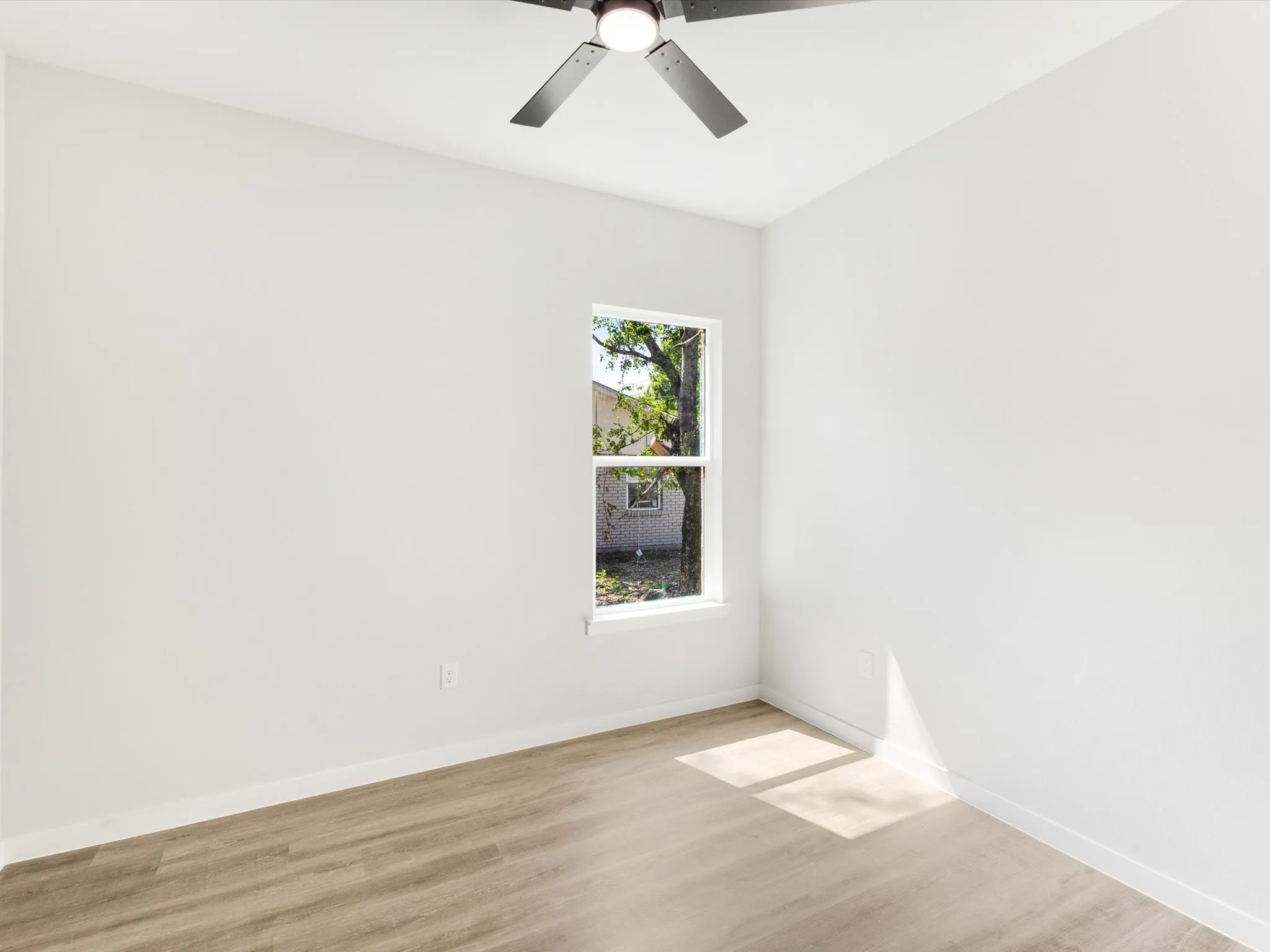 White painted walls with wood-finish flooring, featuring a window and a ceiling fan