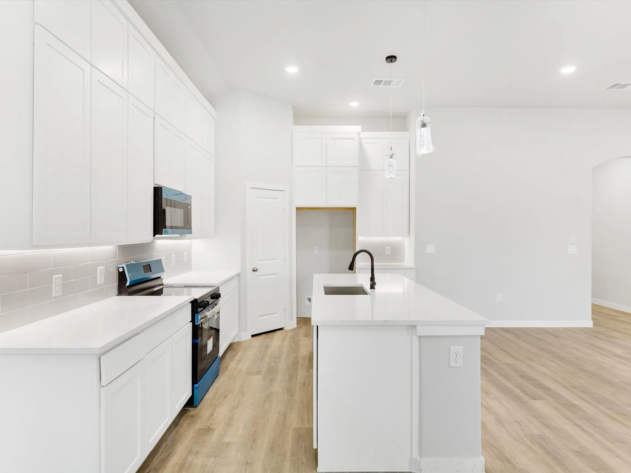 Contemporary kitchen showcasing white cabinetry throughout, quartz countertops, a center island with waterfall edge, stainless steel appliances including a dishwasher and range, subway tile backsplash, pendant lighting, wood-finish flooring, and an open layout with ample natural light from recessed ceiling fixtures