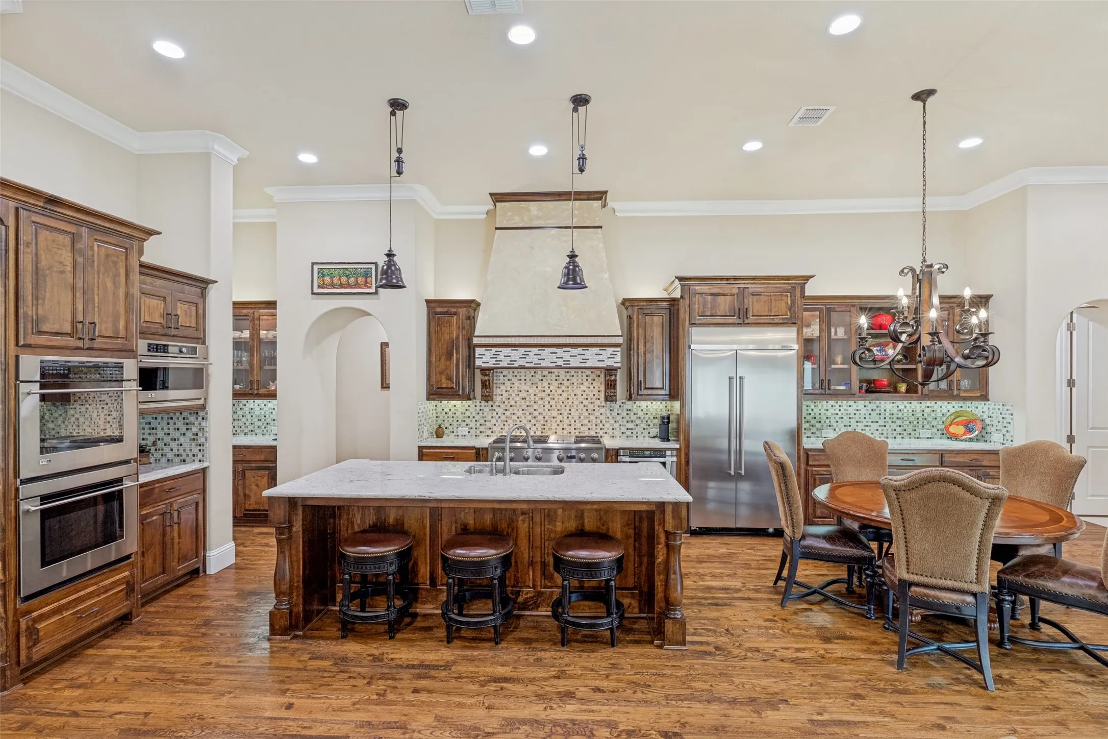 This chef's kitchen will please all the cooks in the family.  Pull up a stool at the oversized island and grab a quick snack or join in the kitchen activities.  A pair of pendant lights hang above the island and abundant recessed lights add plenty of illumination. Under counter and above cabinet lighting is a plus.  Along with the island, abundant stained cabinets with granite countertops and iron hardware provide storage and plentiful space for food prep and serving.
