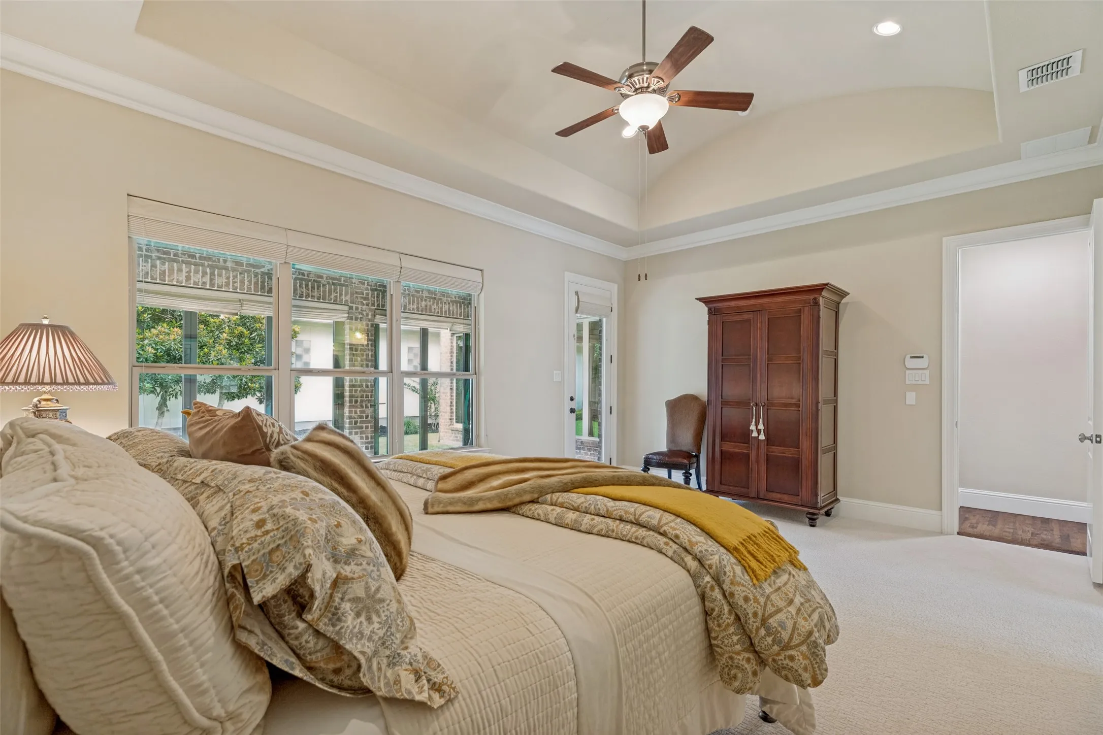 Located at the back of the home, the primary bedroom is adjacent to the enclosed patio with windows that look out through the patio to the green space in the back yard.  A door leads to the patio.  Recessed lights are in the raised ceiling.