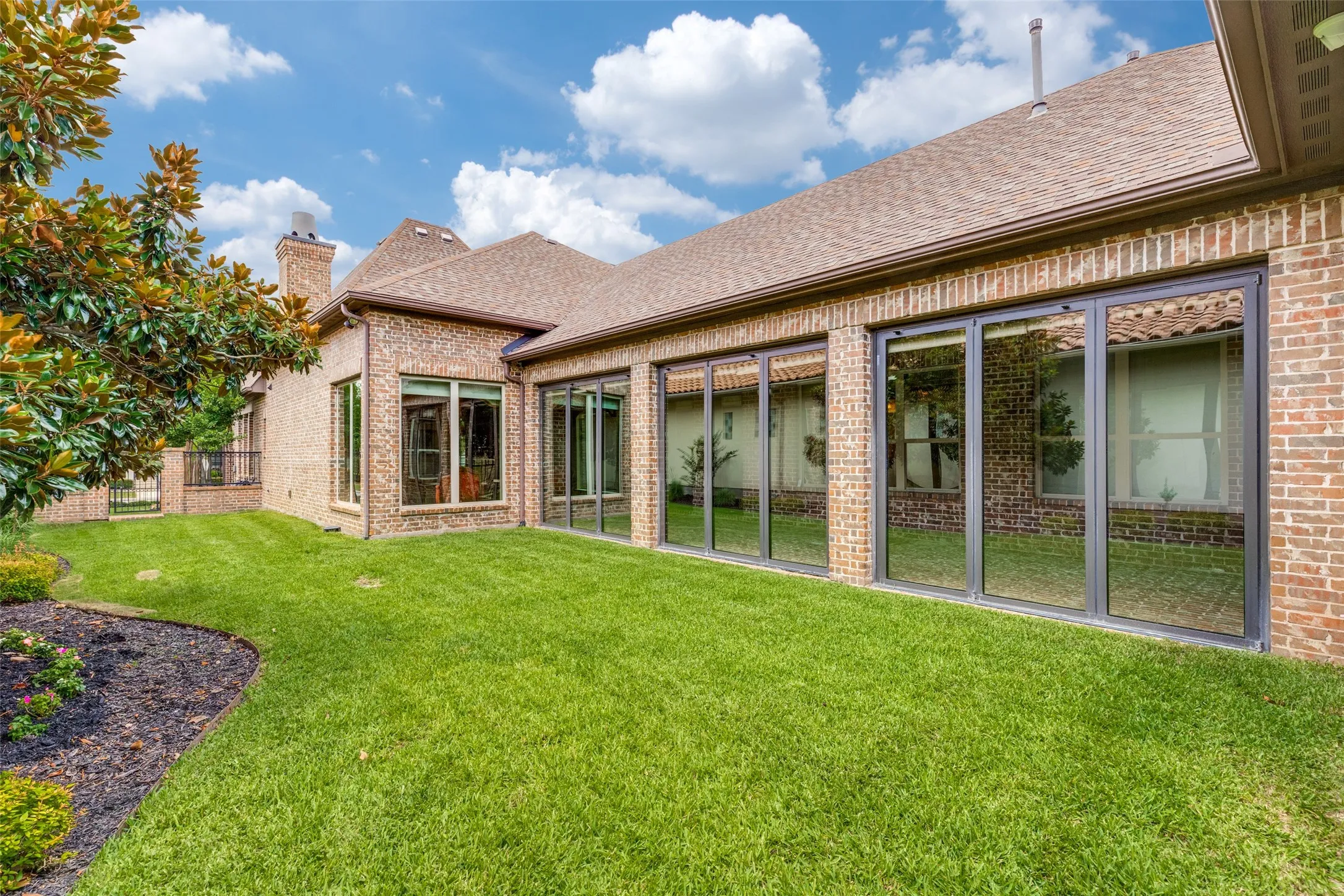 Owners can enjoy the outdoors with the private side yard.  There is plenty of space for pets and play in the generous grassy area.  An attractive landscaping bed decorates the area, and options for additional outside amenities are endless here.  Brick half-walls topped with iron railings and an iron gate lead to the front of the home.  Notice the brick chimney that adds to the appeal of the exterior.