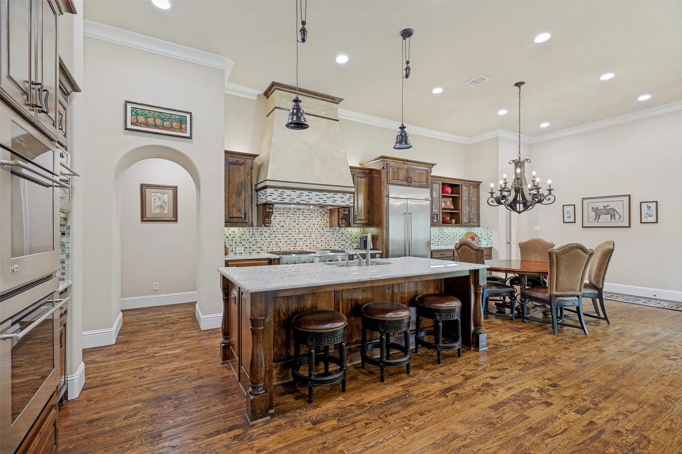 Wood floors flow through the kitchen and breakfast area and crown molding dresses up the ceiling.  A handsome vent hood is above the GE Monogram commercial style gas cooktop and a built-in KitchenAid refrigerator/freezer is also part of the appliance package.  An arched casement leads to the guest bedroom, access to the utility room and a storage closet or second pantry.