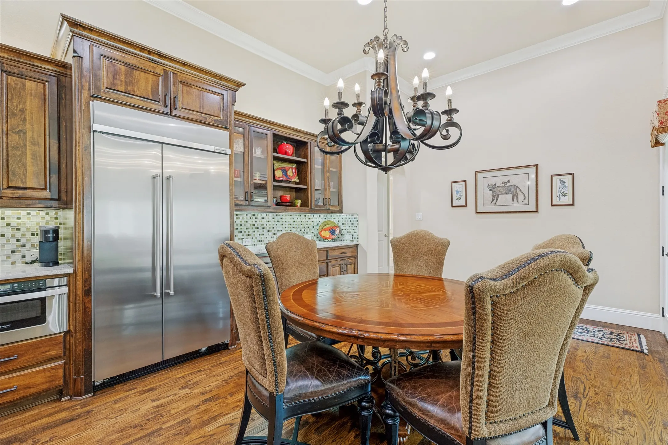The casual dining area is anchored by a handsome ornate iron chandelier.  A hutch with glass fronts in the upper cabinets adds to the storage in the kitchen area.  The wood floors extend into the hallway with access to the primary bedroom on one side and to a door to the sun porch/patio on the other.