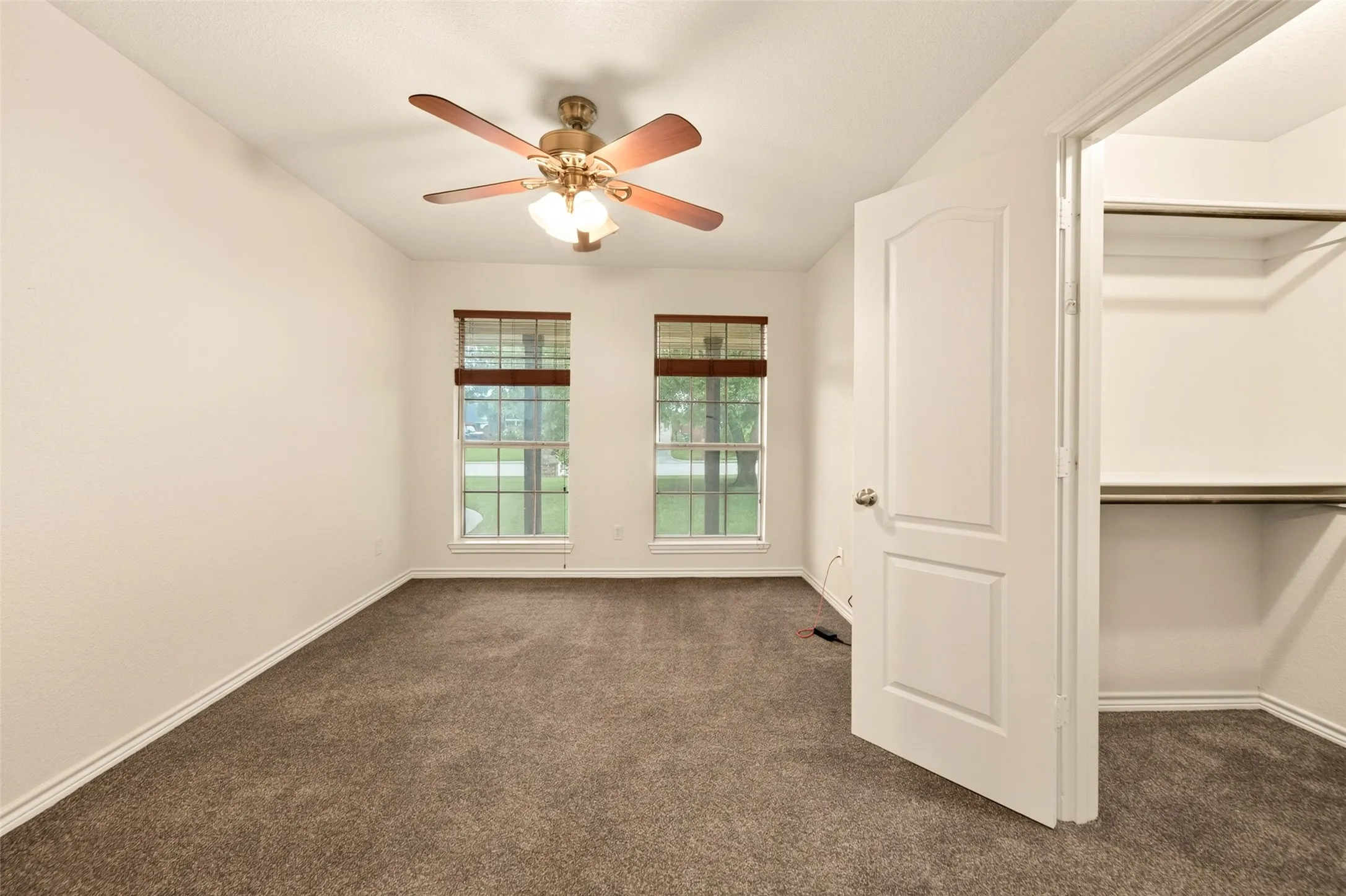 Bedroom featuring dark grey tone carpet flooring, a ceiling fan with integrated lighting, two windows with wood-tone blinds, and a closet with shelving and a hanging rod