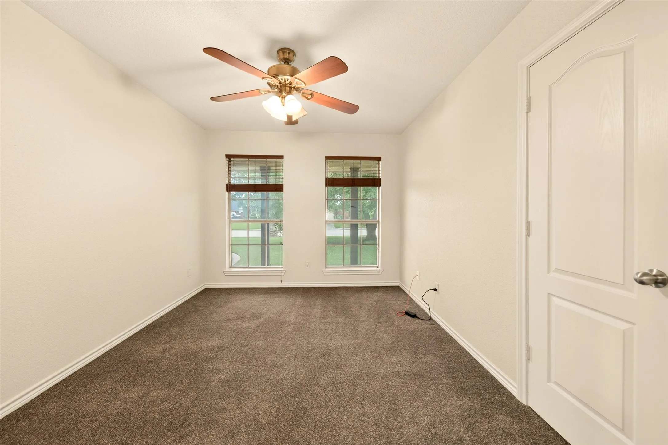 Grey carpeted interior space featuring two windows with horizontal blinds, a ceiling fan with integrated lighting, and a paneled interior door to closet.