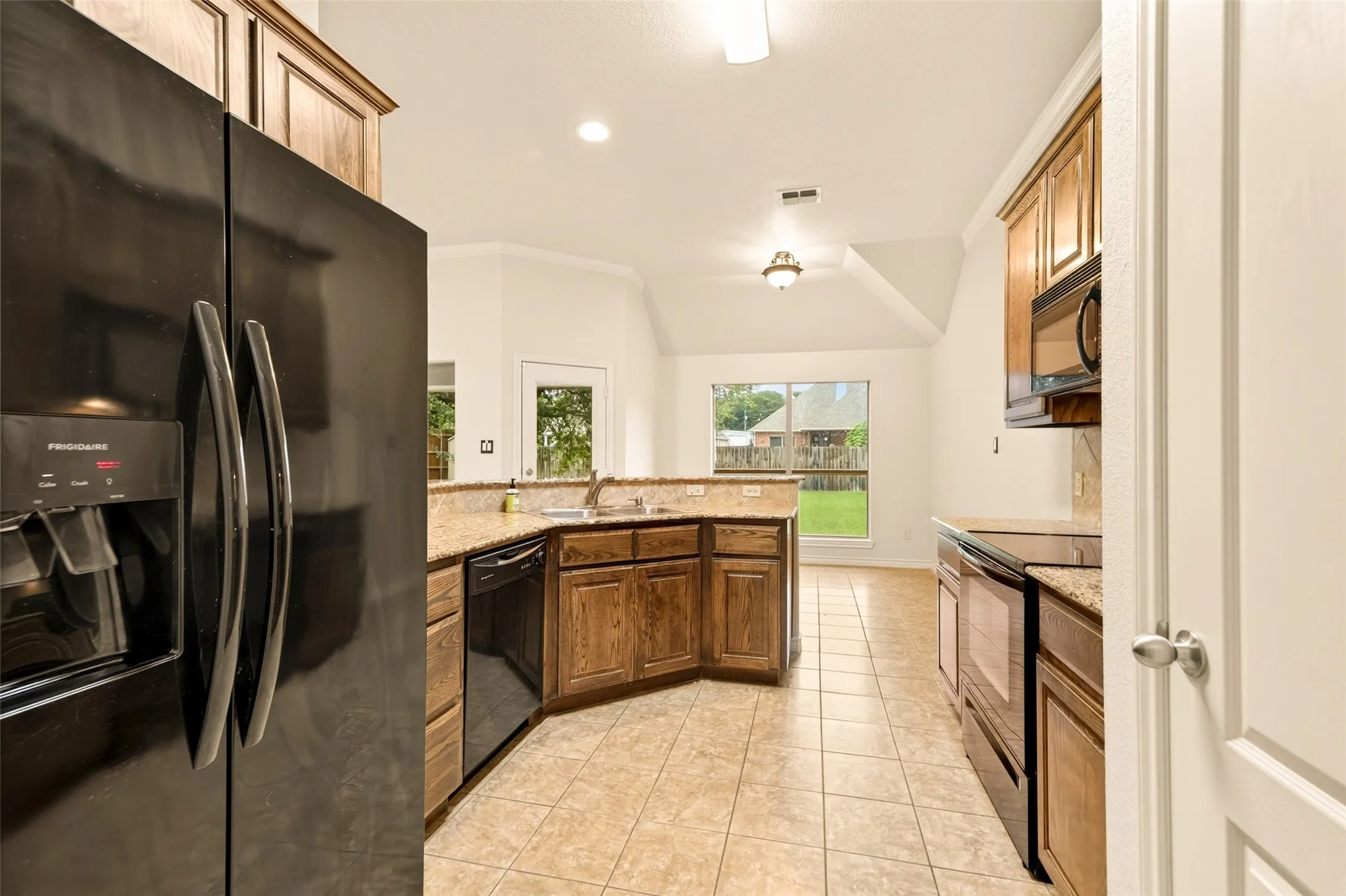 Kitchen featuring wood cabinetry, granite countertops, tile flooring, and integrated black appliances