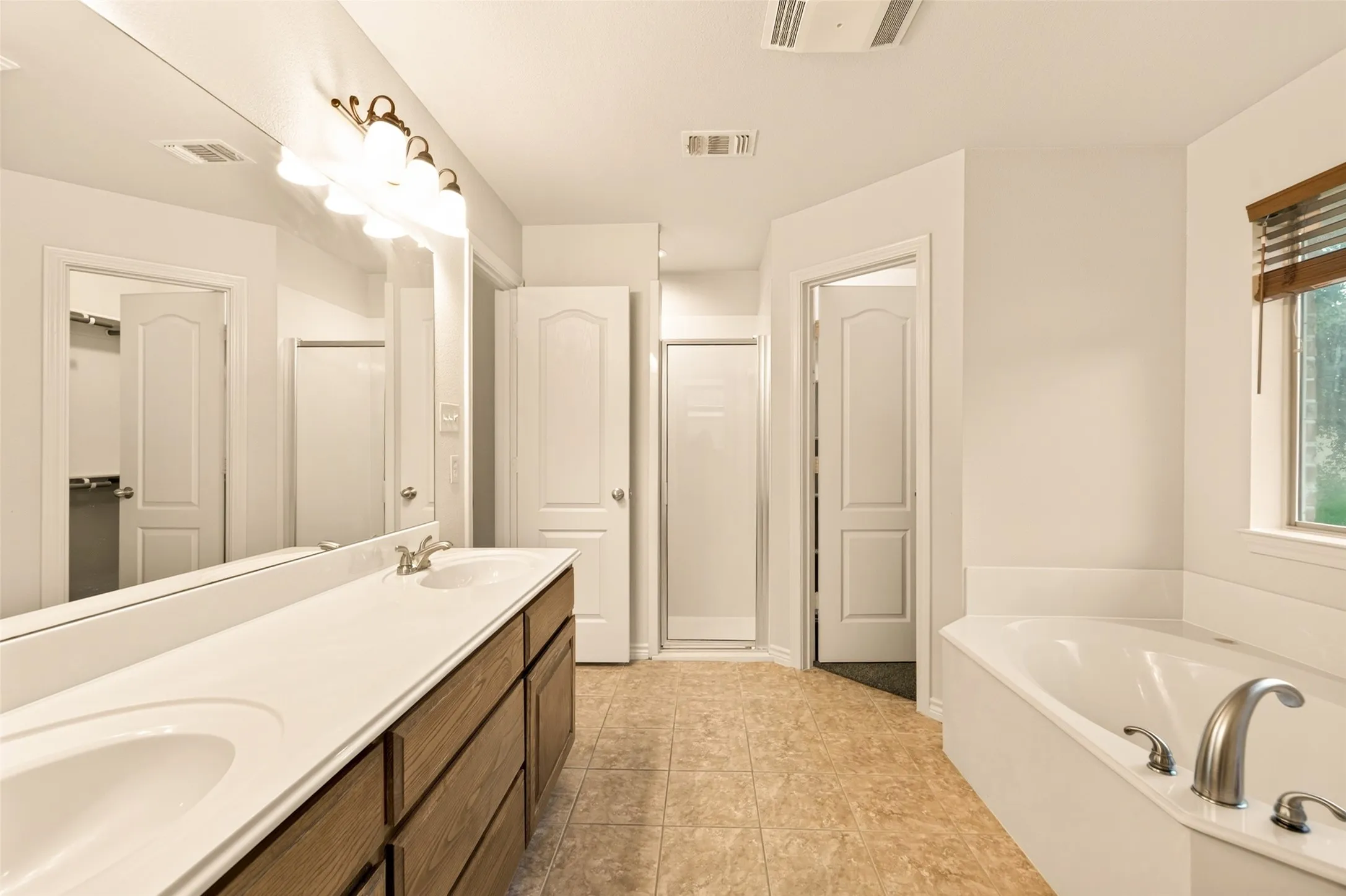 Bathroom featuring a double vanity with wood-finish cabinetry, a large soaking tub, and a separate shower enclosure