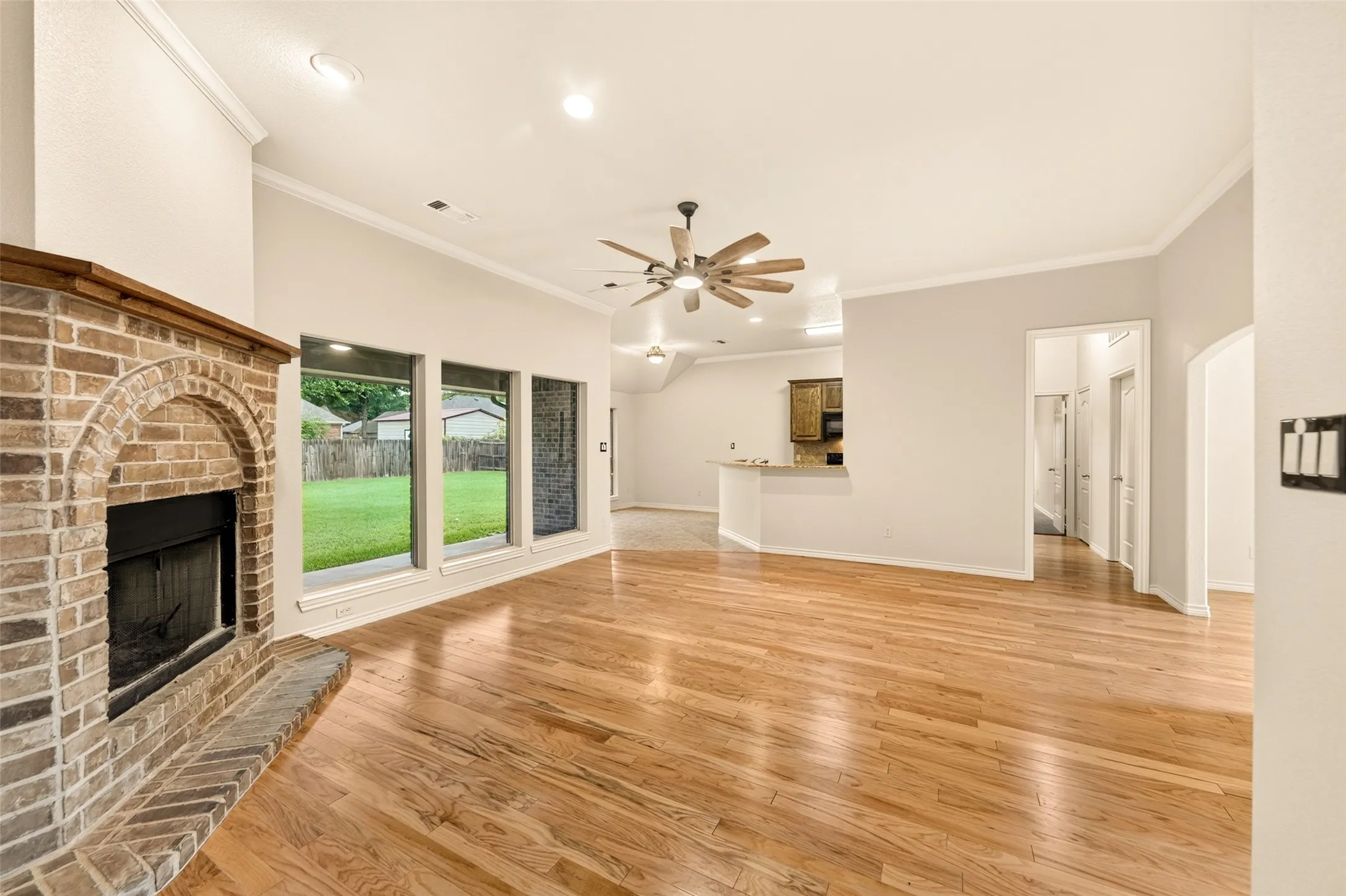 Living area featuring wood-finish flooring, a brick fireplace with a hearth, and a vaulted ceiling with crown molding