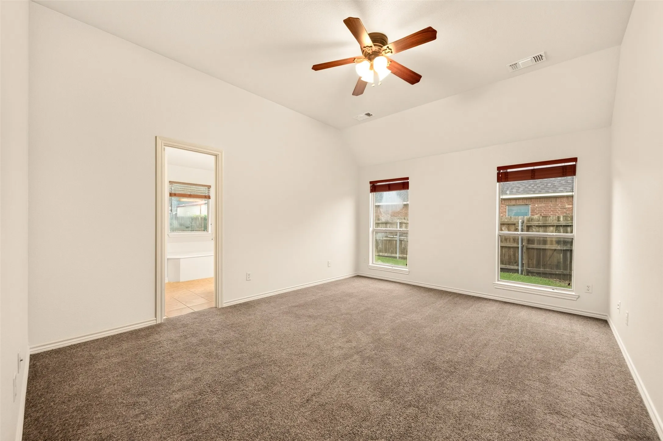 Grey carpeted primary bedroom with vaulted ceilings