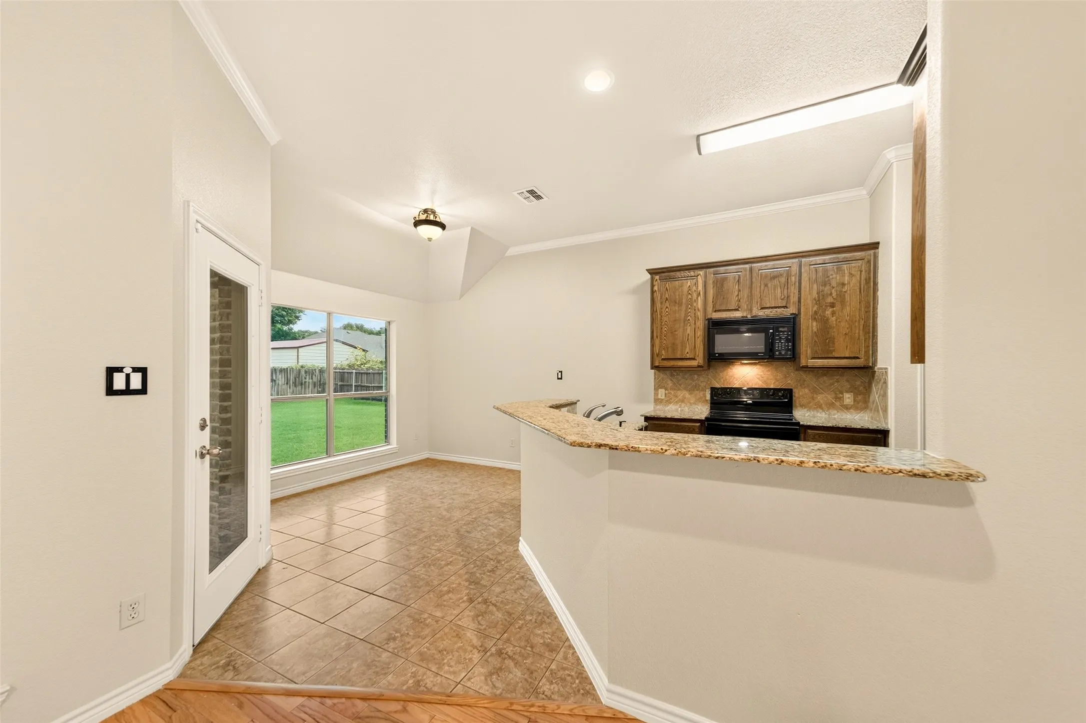 Kitchen area with granite countertops, wood cabinetry, built-in microwave, and tile backsplash