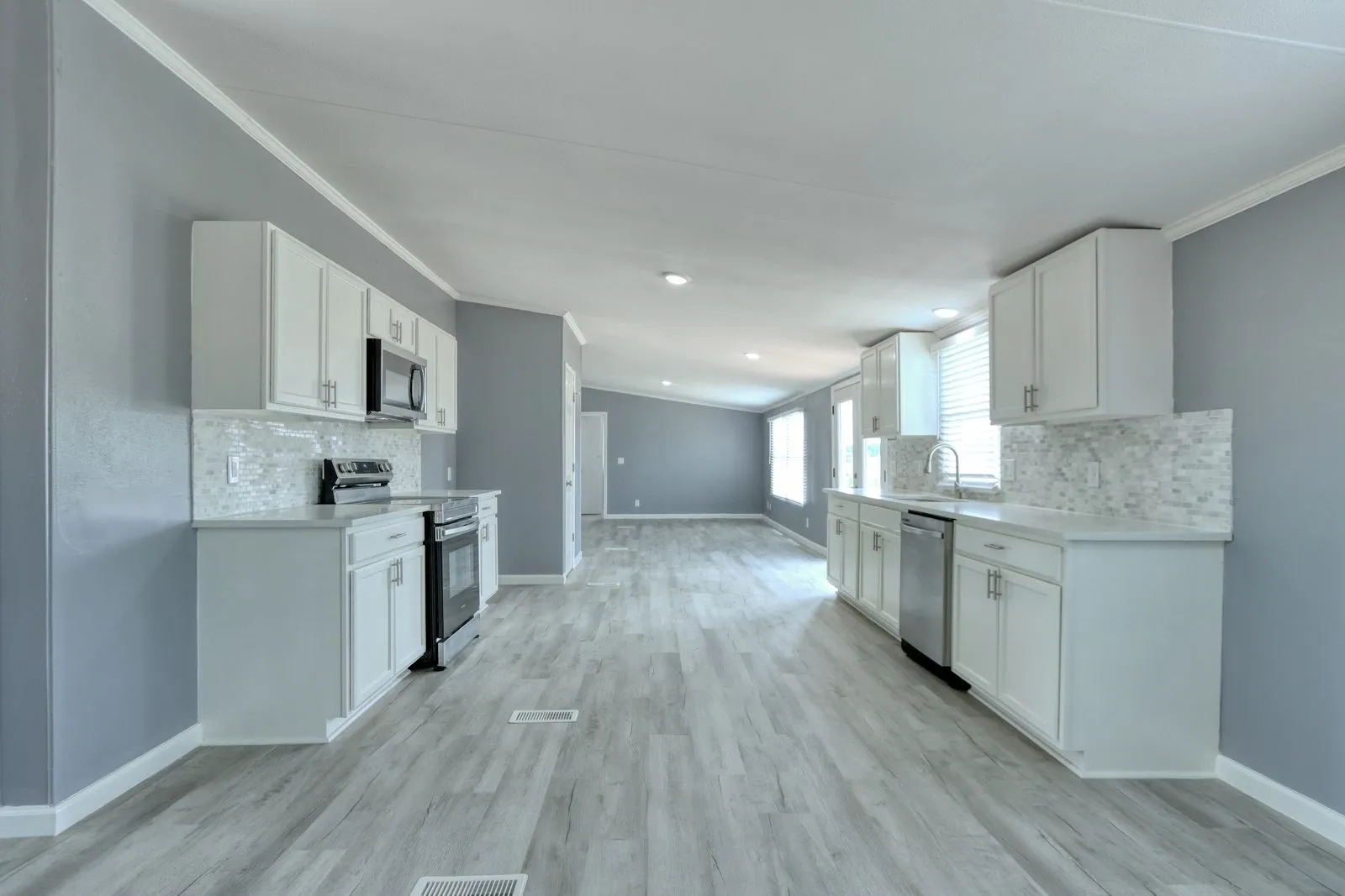 Kitchen featuring white cabinetry, light countertops, a mosaic tile backsplash, stainless steel appliances, and wood-finish flooring