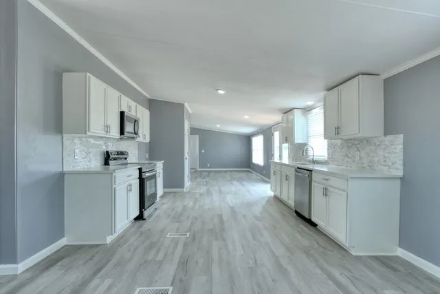 Open-concept kitchen featuring white shaker cabinetry, stainless steel appliances, light-toned countertops, and a full tile backsplash