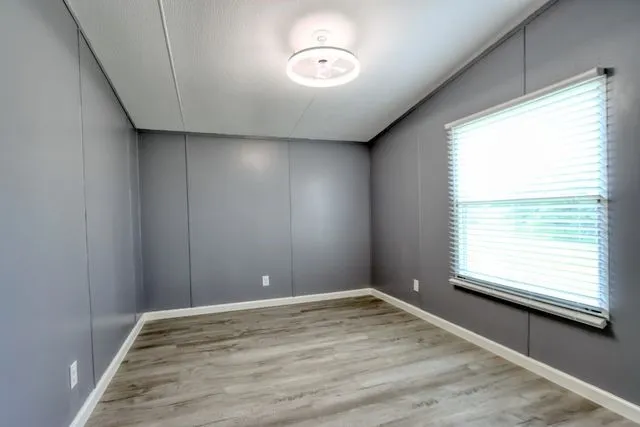 Room featuring grey wall paneling, light wood-finish flooring, and white baseboards