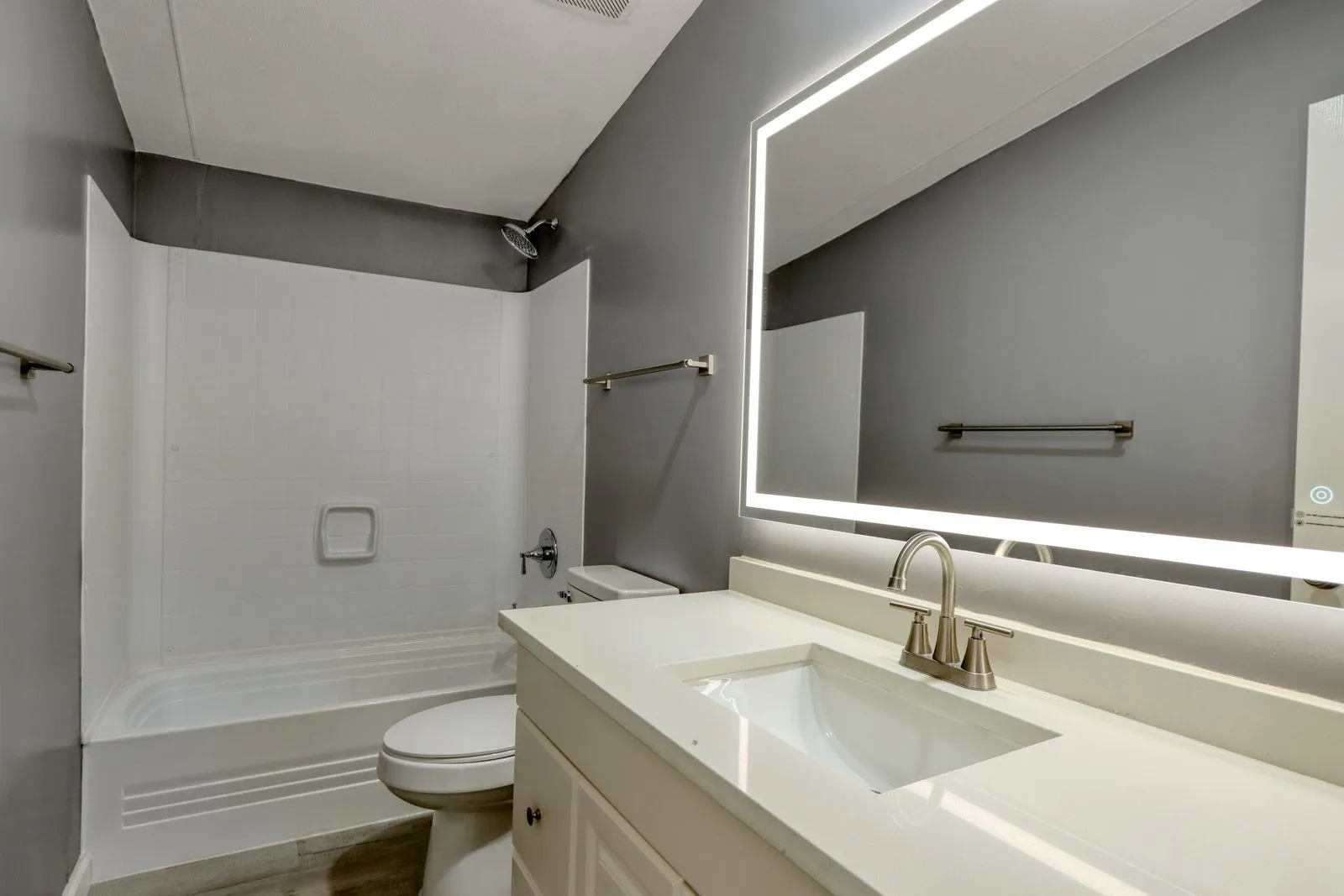 Bathroom featuring a contemporary lighted mirror, white vanity with integrated sink, brushed nickel faucet, and a white tub/shower combination