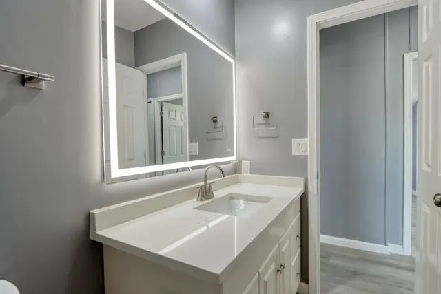 Bathroom vanity featuring a quartz countertop, integrated sink, brushed nickel faucet, and an illuminated mirror
