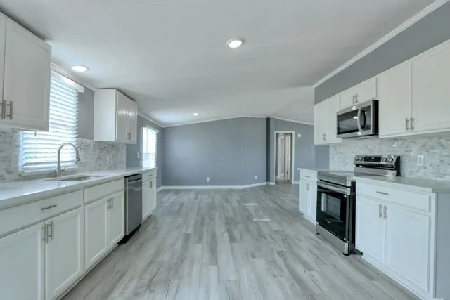 Modern kitchen featuring white cabinetry, light-toned countertops, a mosaic tile backsplash, stainless steel appliances, and wood-finish flooring