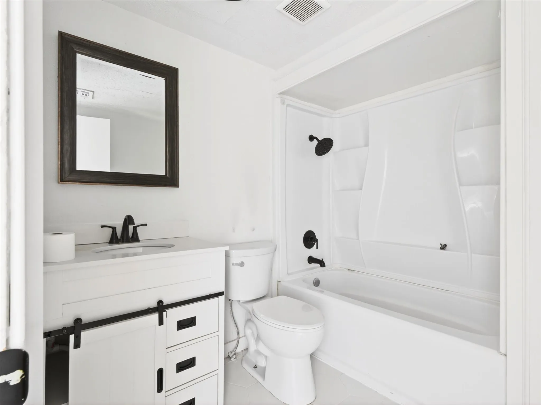 Bathroom featuring a white vanity with a sliding barn door cabinet, three drawers, and matte black hardware