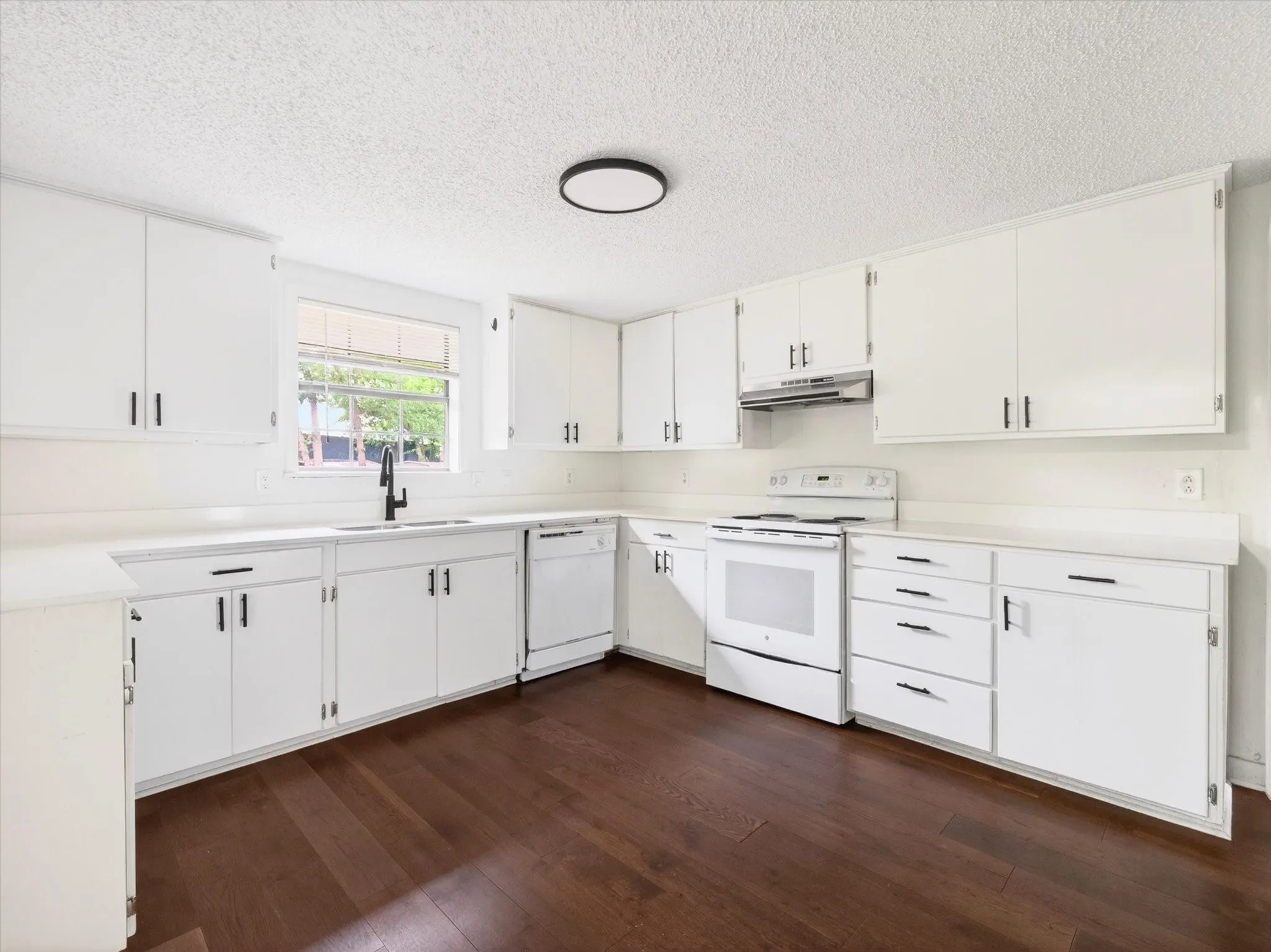 Kitchen featuring dark wood-finish flooring, white cabinetry, a window over the sink, white appliances, and a circular ceiling light fixture