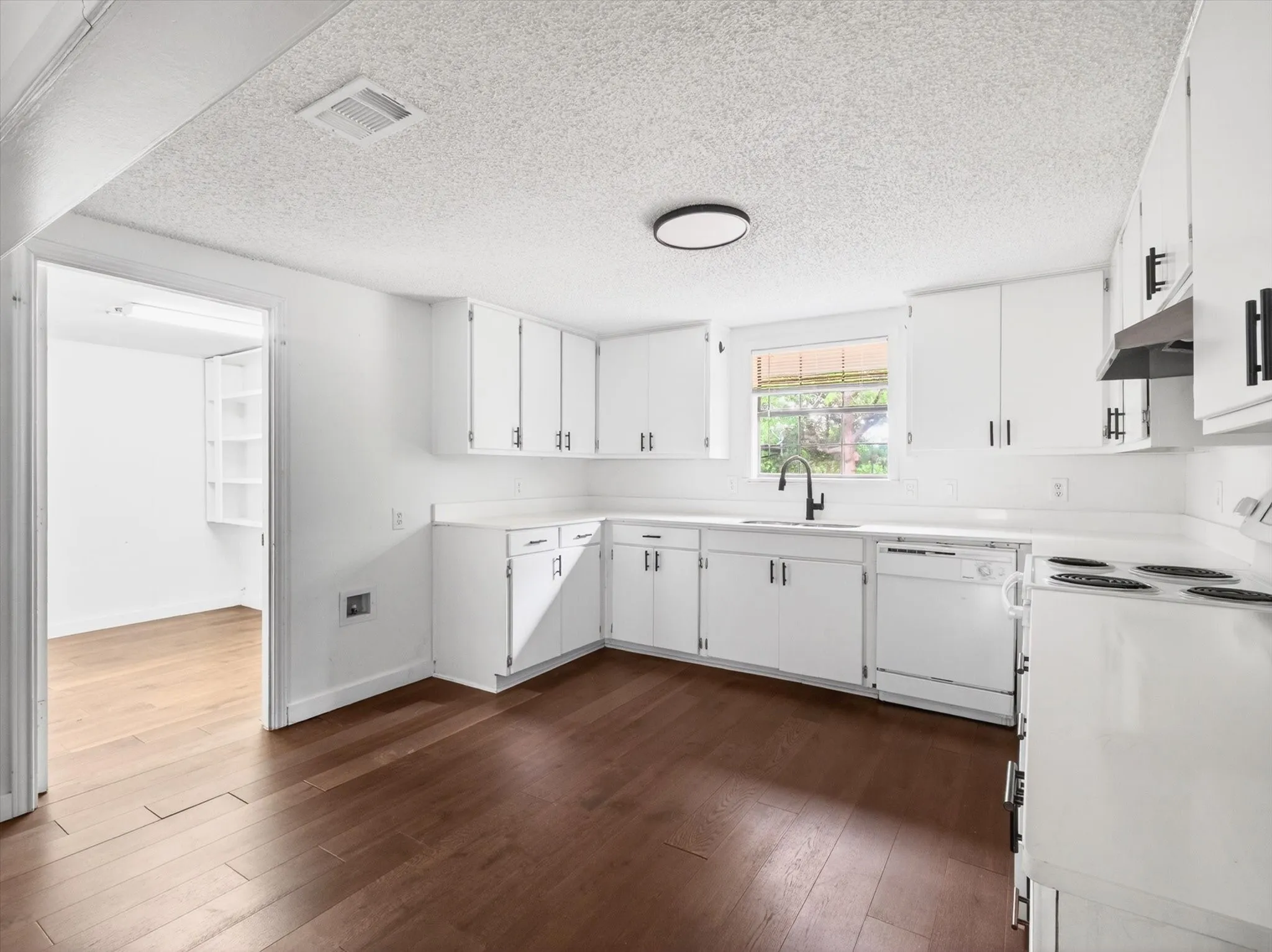 Kitchen featuring an L-shaped counter, white cabinetry with black hardware, a black faucet, a white dishwasher, and wood-finish flooring