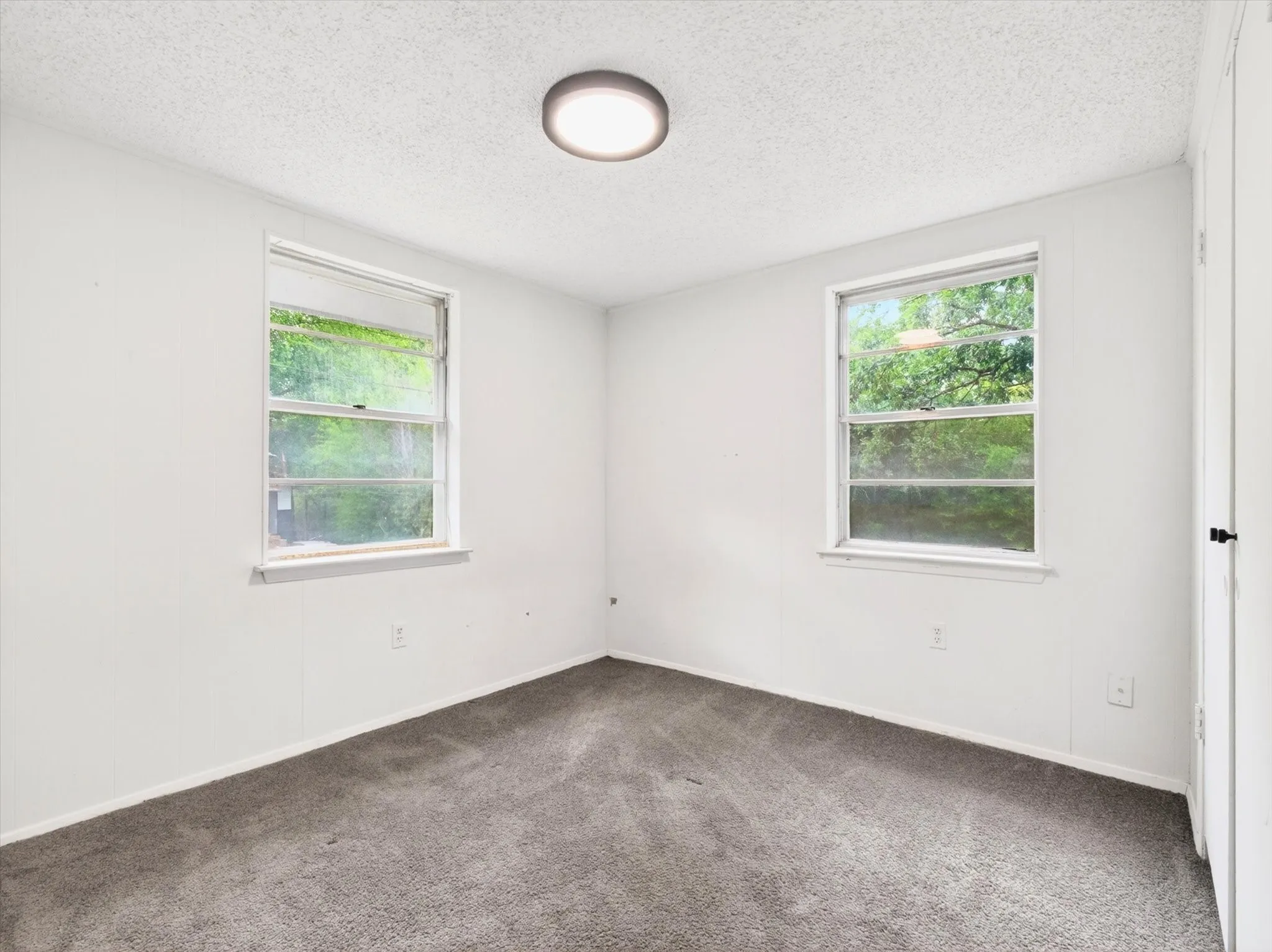 Room featuring two windows, neutral wall finishes, grey carpet flooring, a flush-mount ceiling light fixture, and a white interior door with black hardware