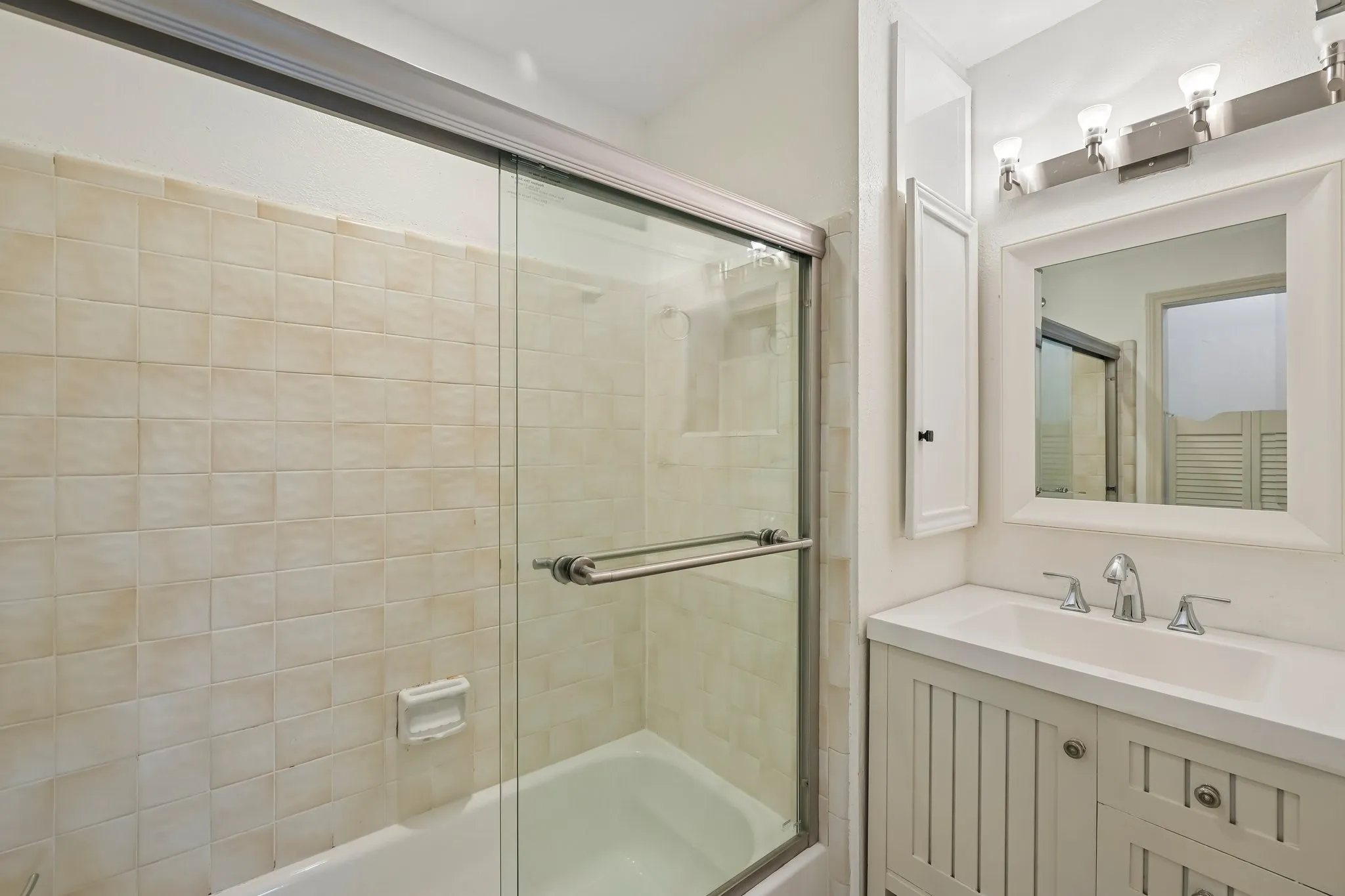 Bathroom featuring a tub with glass shower enclosure, a vanity with integrated sink, a framed mirror, and an overhead light fixture