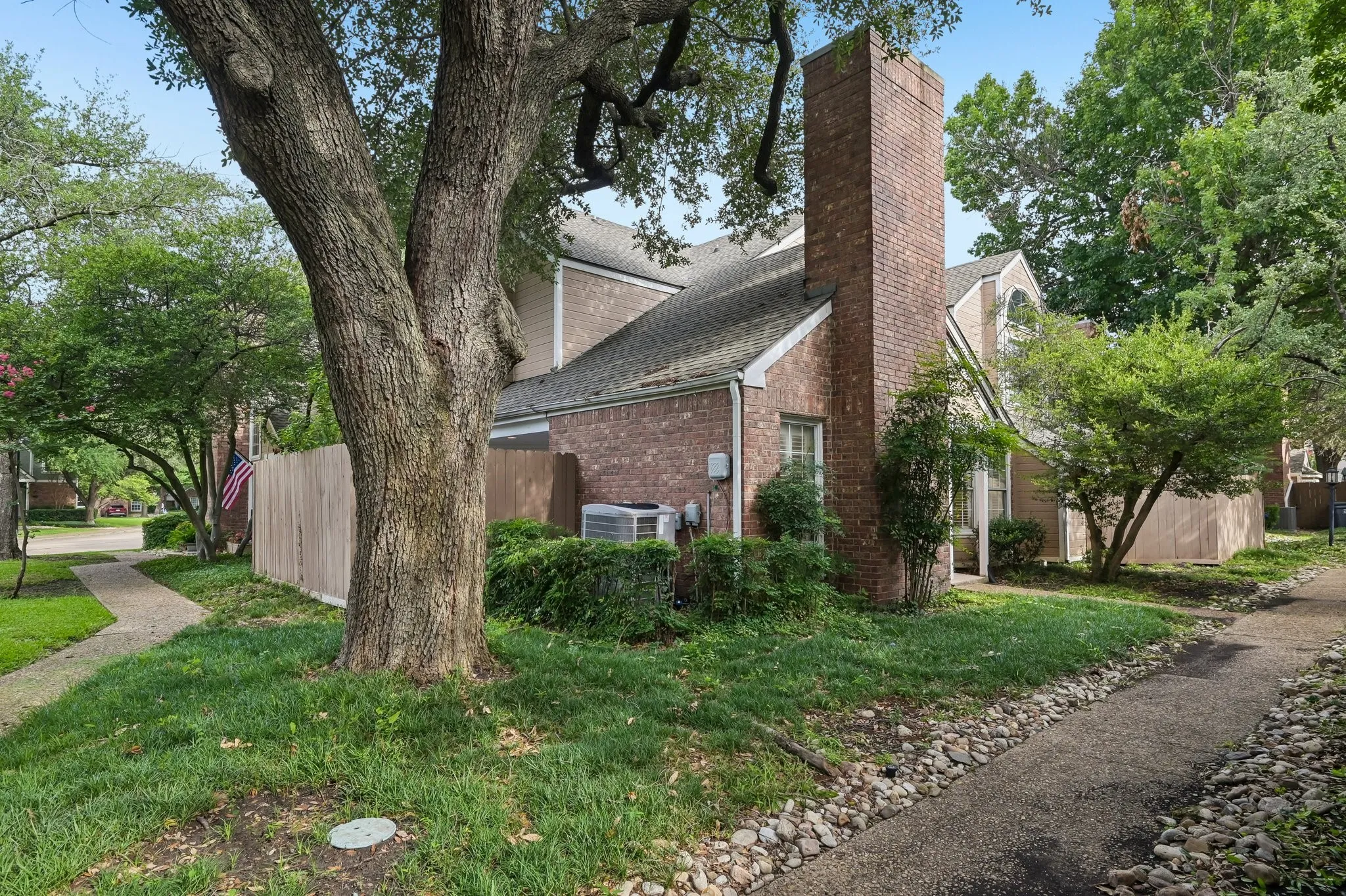 Brick exterior with a prominent chimney, surrounded by mature trees and established landscaping