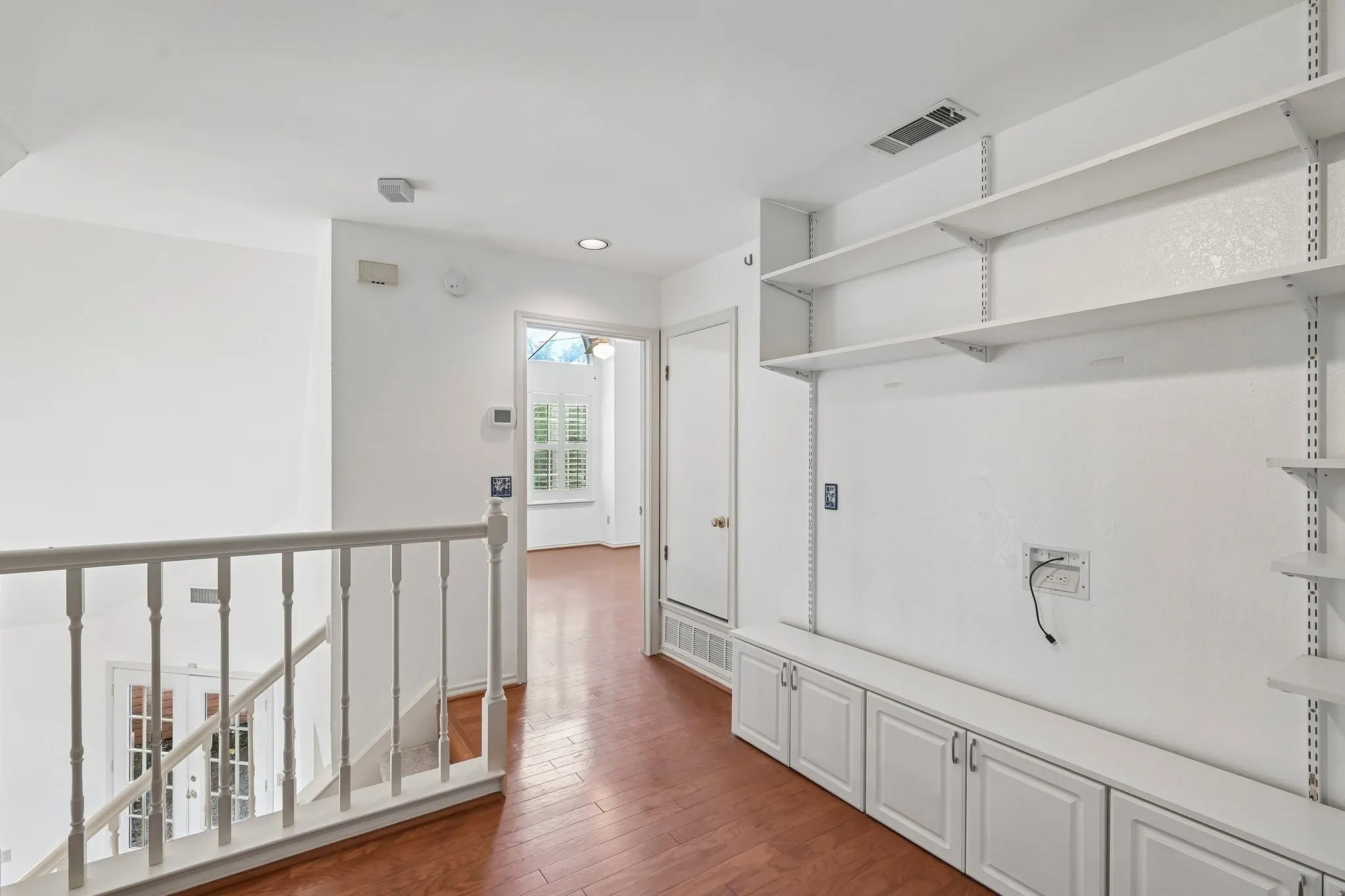 Loft featuring wood-finish flooring, built-in shelving, lower cabinetry, and a white baluster railing overlooking a lower level