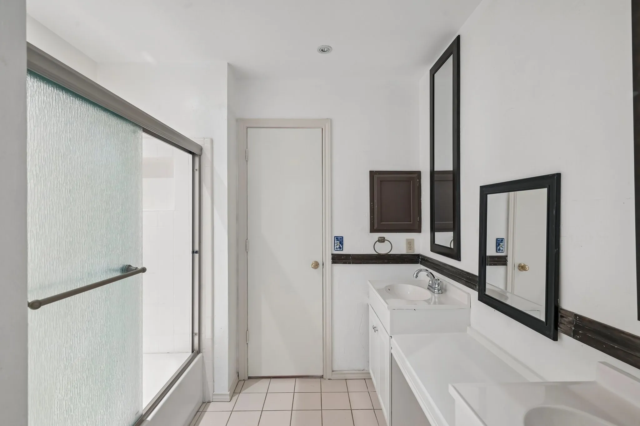 Bathroom with a sliding glass shower door, dual vanities with integrated sinks, framed mirrors, and tile flooring