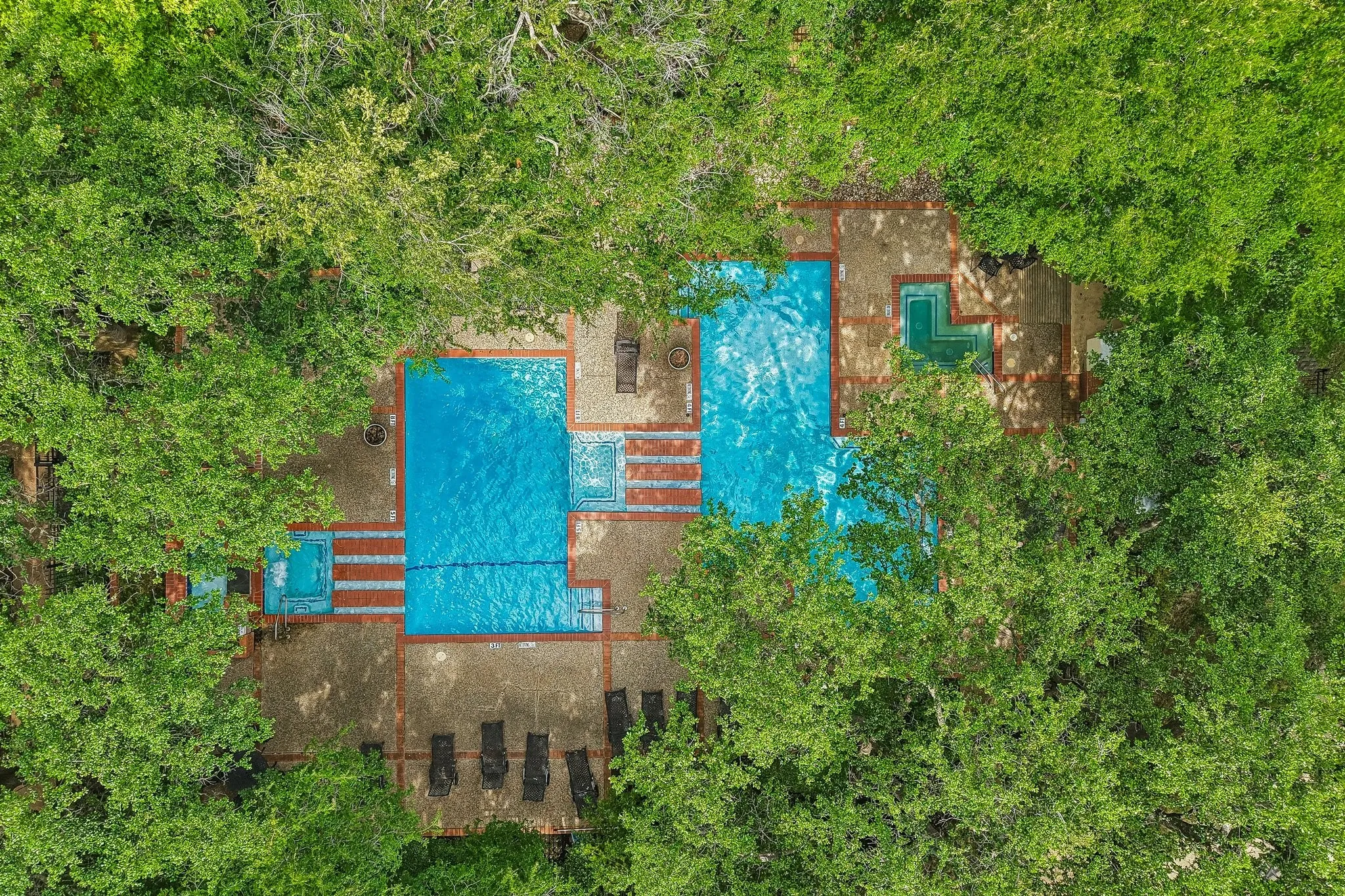 Expansive aquatic area featuring two distinct pools with blue interiors, an integrated spa, and brick-patterned hardscaping