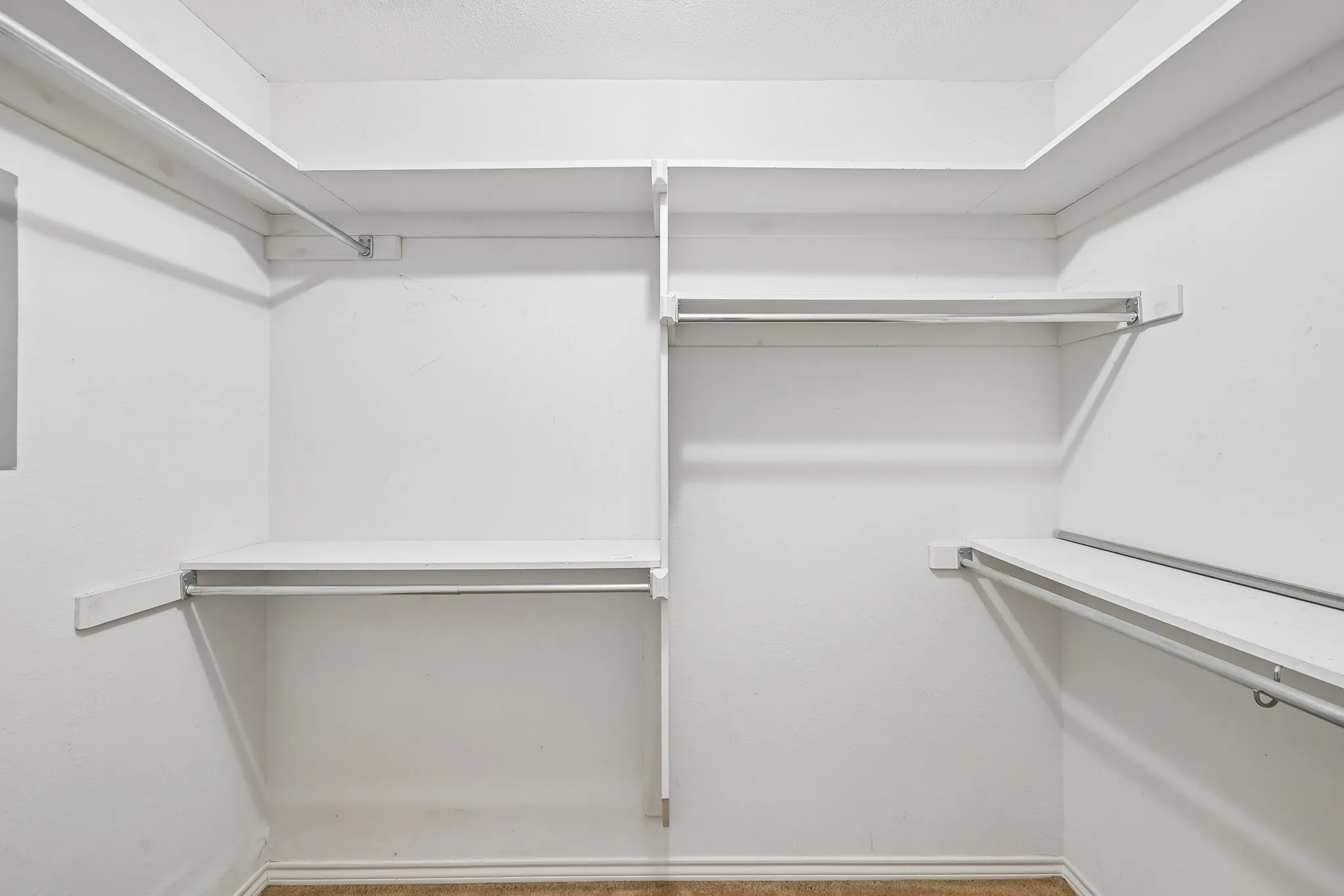Walk-in closet featuring white painted walls, multiple storage shelves, and chrome hanging rods