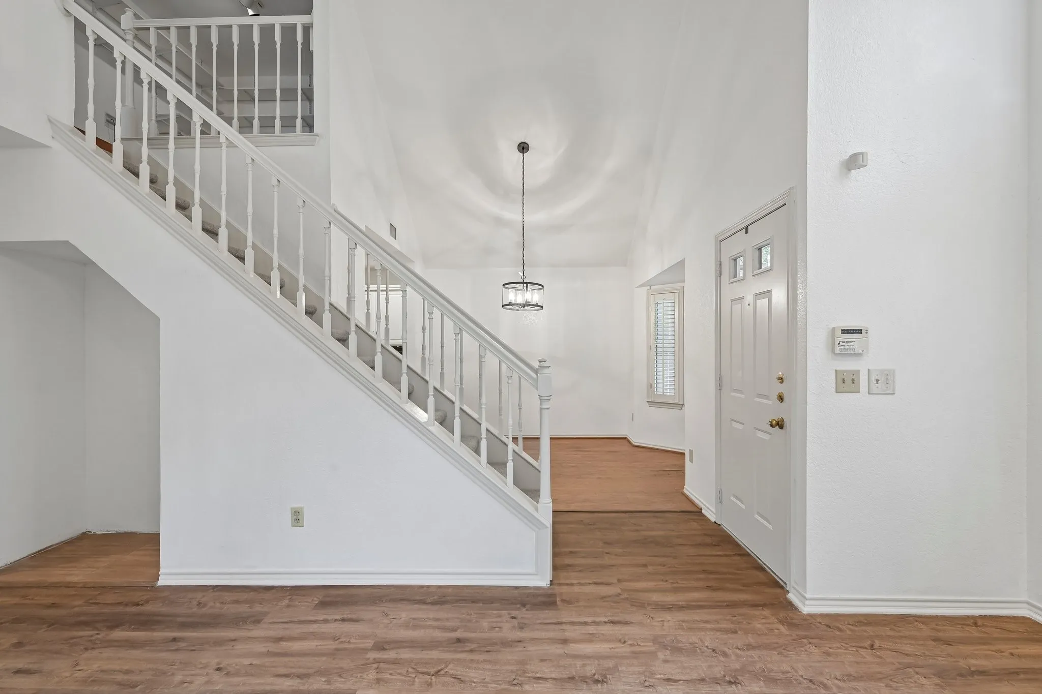 Two-story entryway featuring wood-finish flooring, a white spindle staircase, and a contemporary chandelier