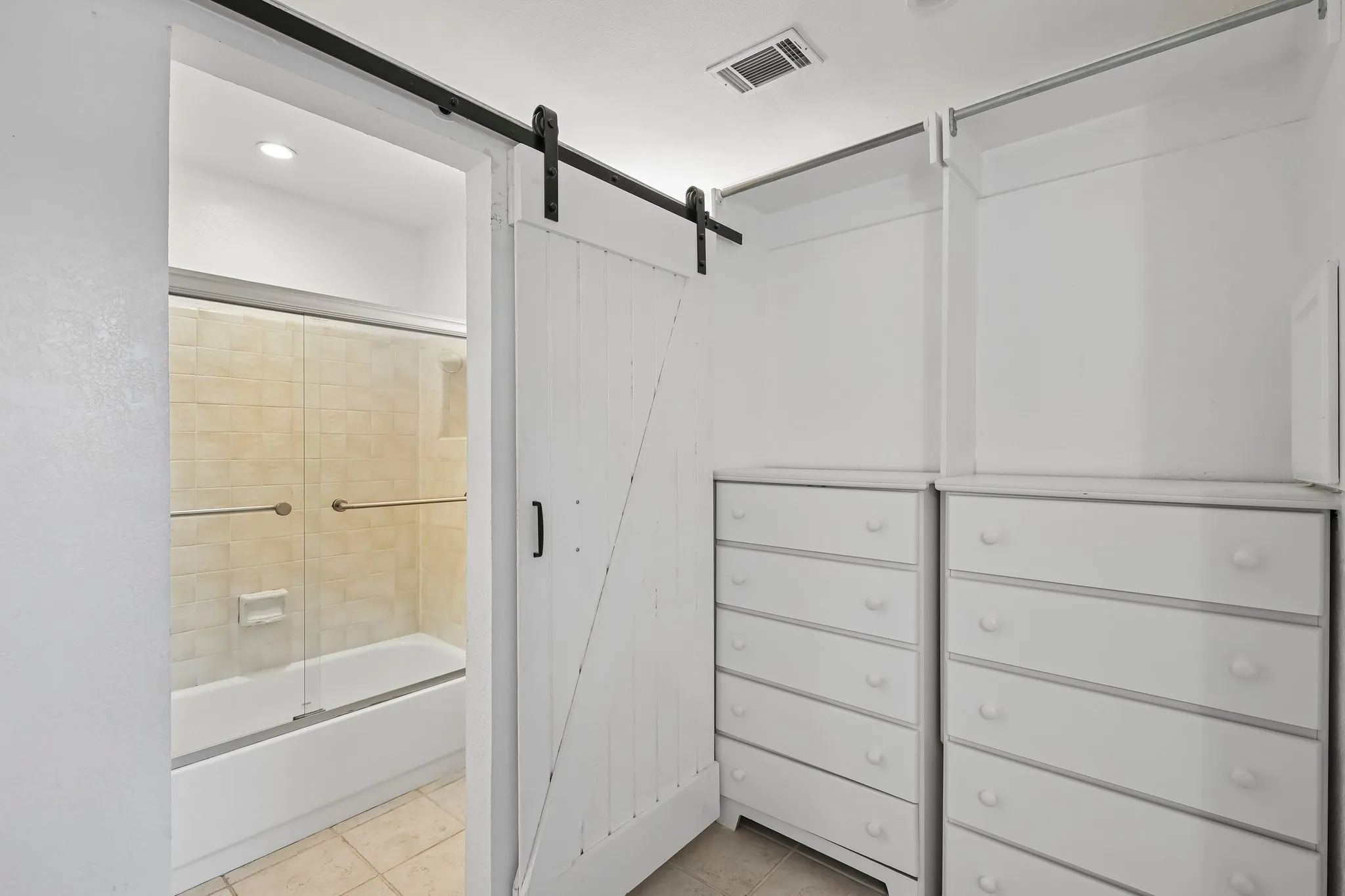 White barn door entry to a bathroom featuring a tub and shower combination with glass sliding doors and neutral tile surround