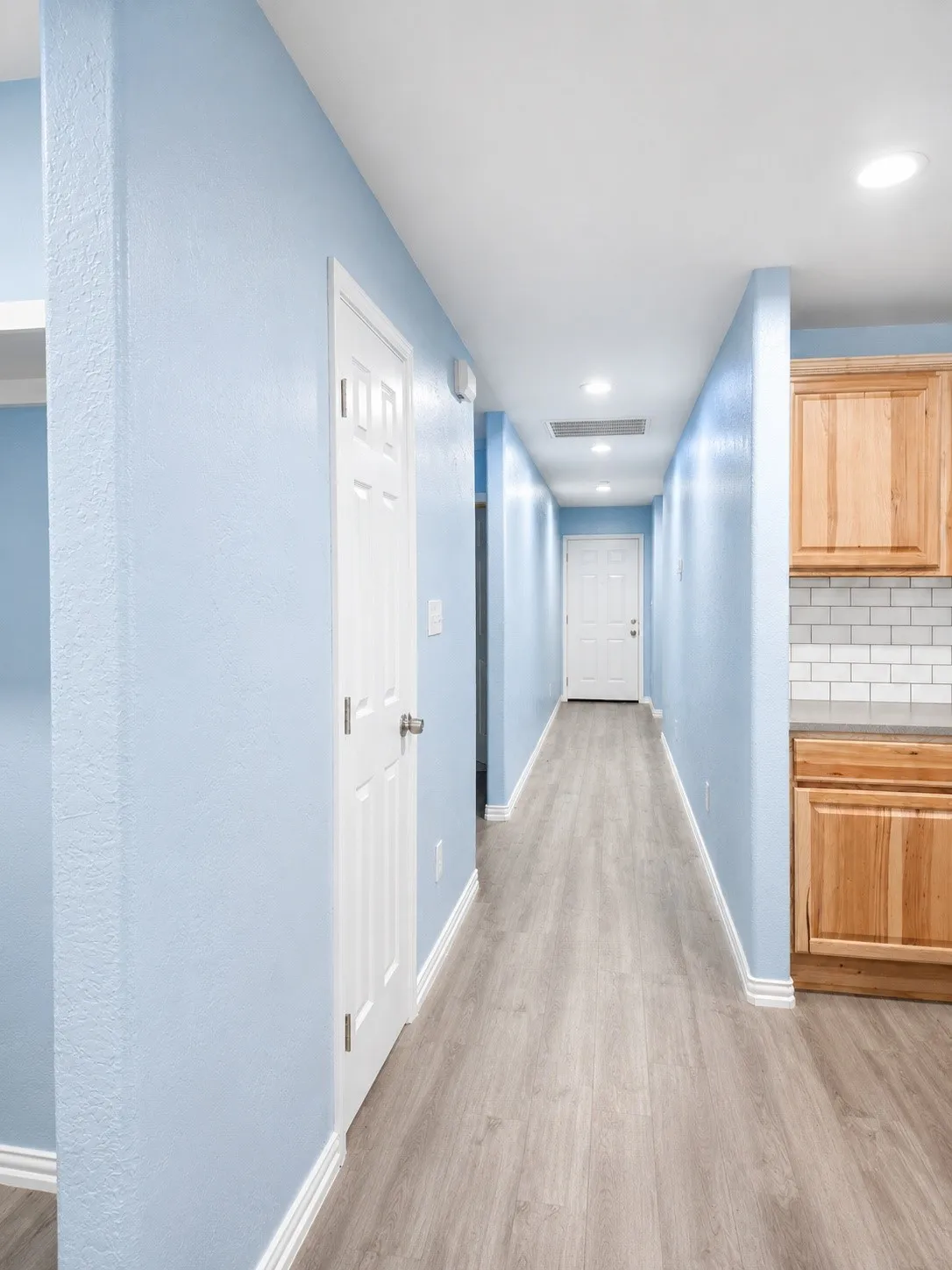 Hallway featuring light blue walls, wood-finish flooring, recessed lighting, and white baseboards