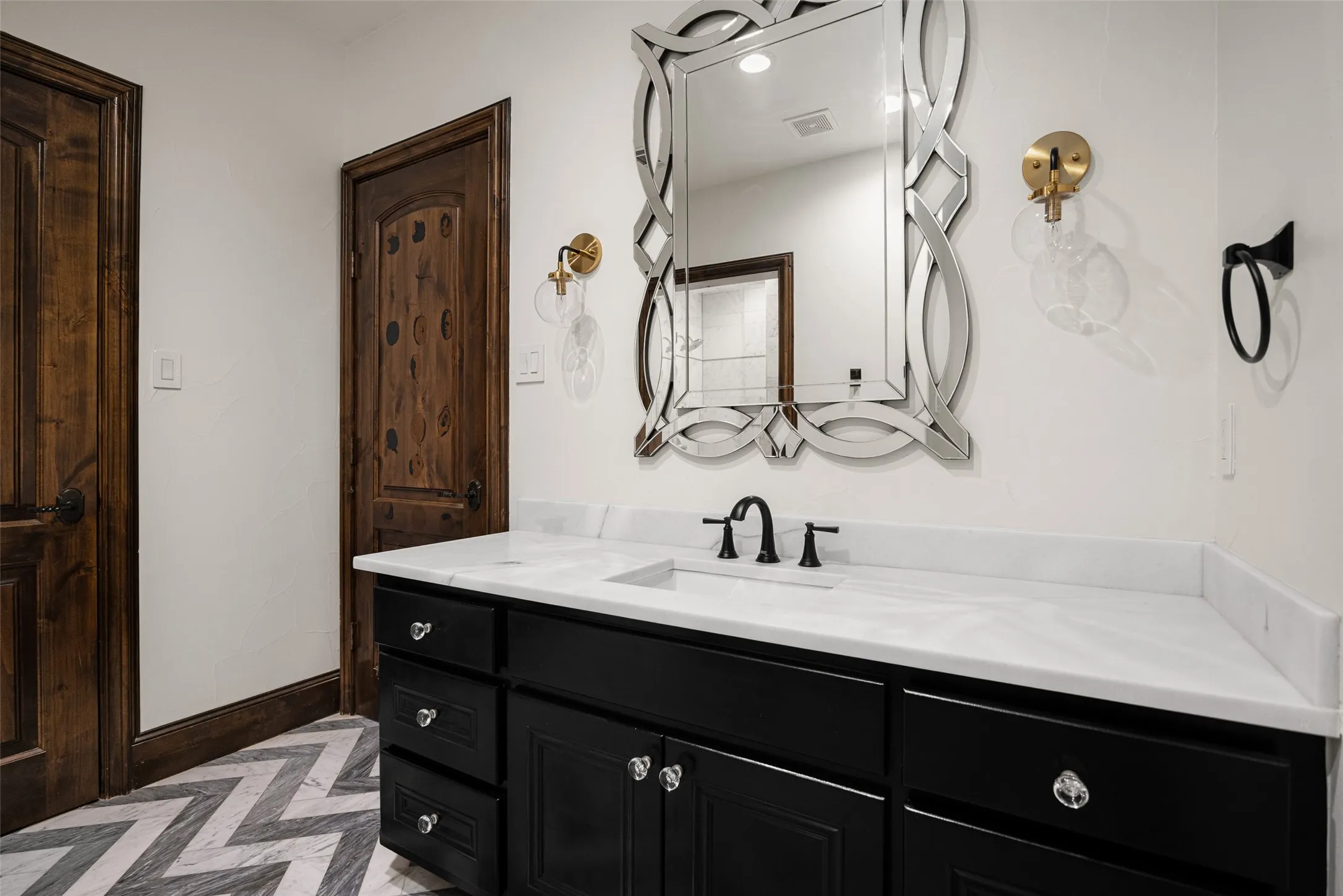 Bathroom featuring a dark wood vanity with clear knob hardware, white countertop with integrated sink, black faucet, and an ornate mirror