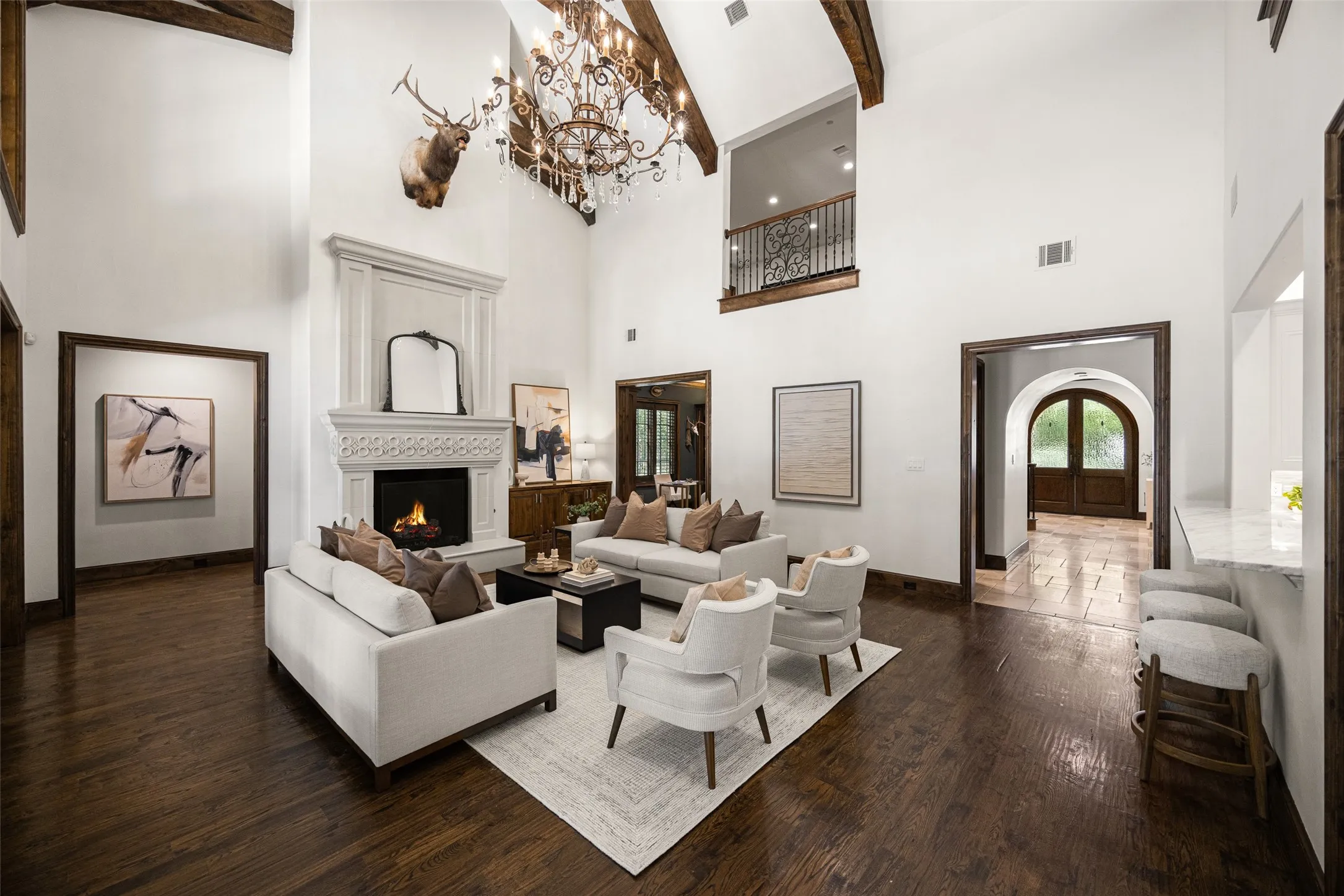Living area featuring vaulted ceilings with exposed wood beams, a stone fireplace with an ornate mantel, dark wood-finish flooring, and an open balcony with wrought iron railing