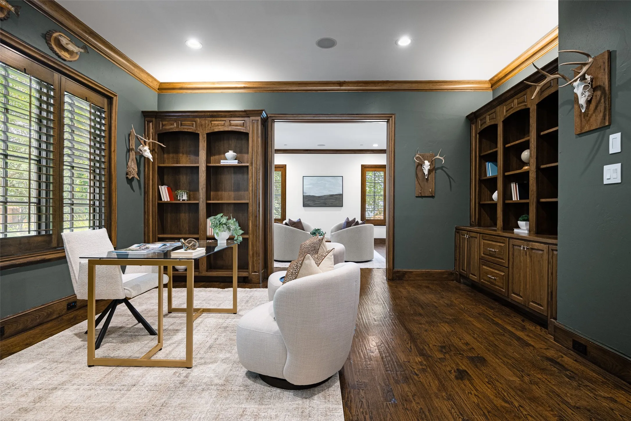 Dedicated interior space featuring dark wood-finish flooring, custom built-in cabinetry, wood plantation shutters, dark wall finishes, and a framed doorway