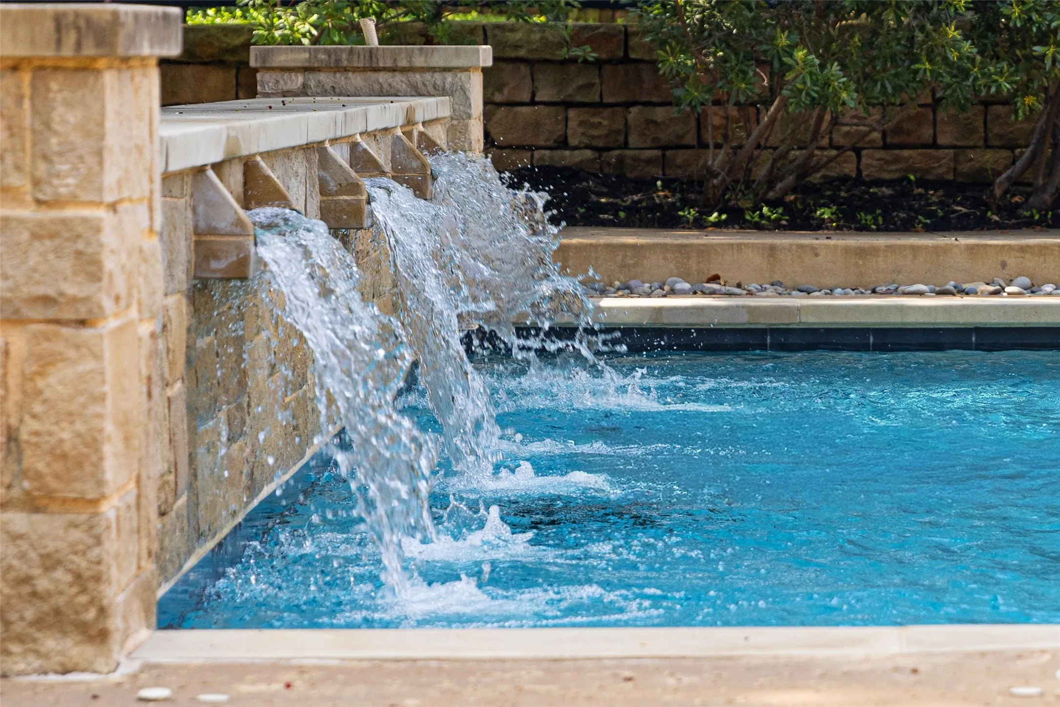 Resort-style pool featuring multiple stone-clad waterfall spillways, blue tile accents, and a perimeter of decorative river rock