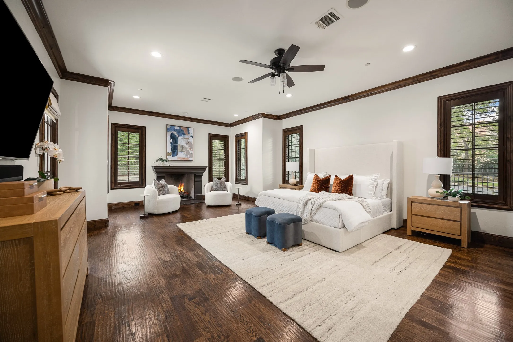 Spacious room featuring rich wood-finish flooring, a traditional fireplace with a stone surround, and extensive crown molding
